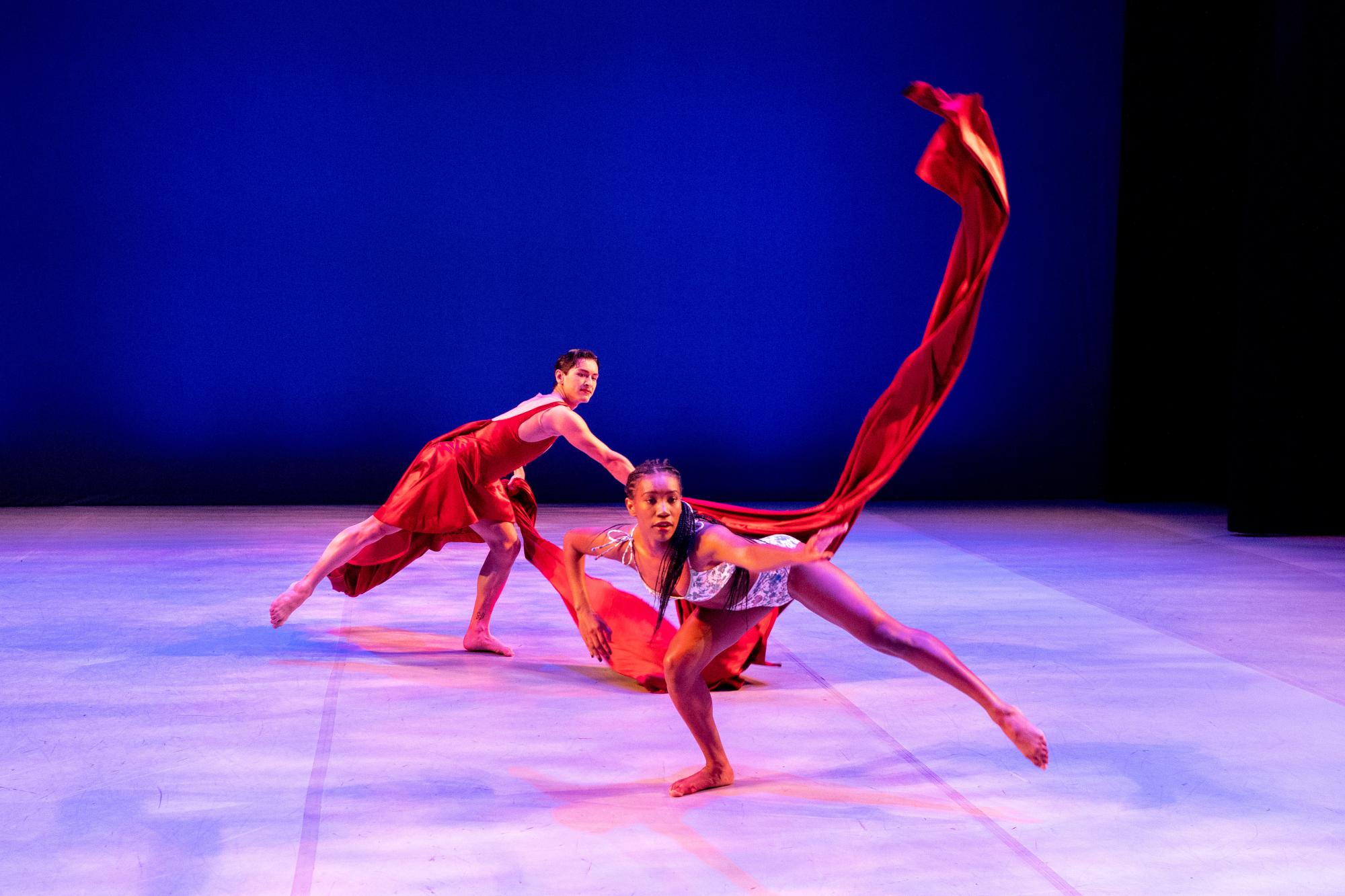 a dancer in a red dress throws his long train of red fabric, lining up with another dancer's outstretched arm