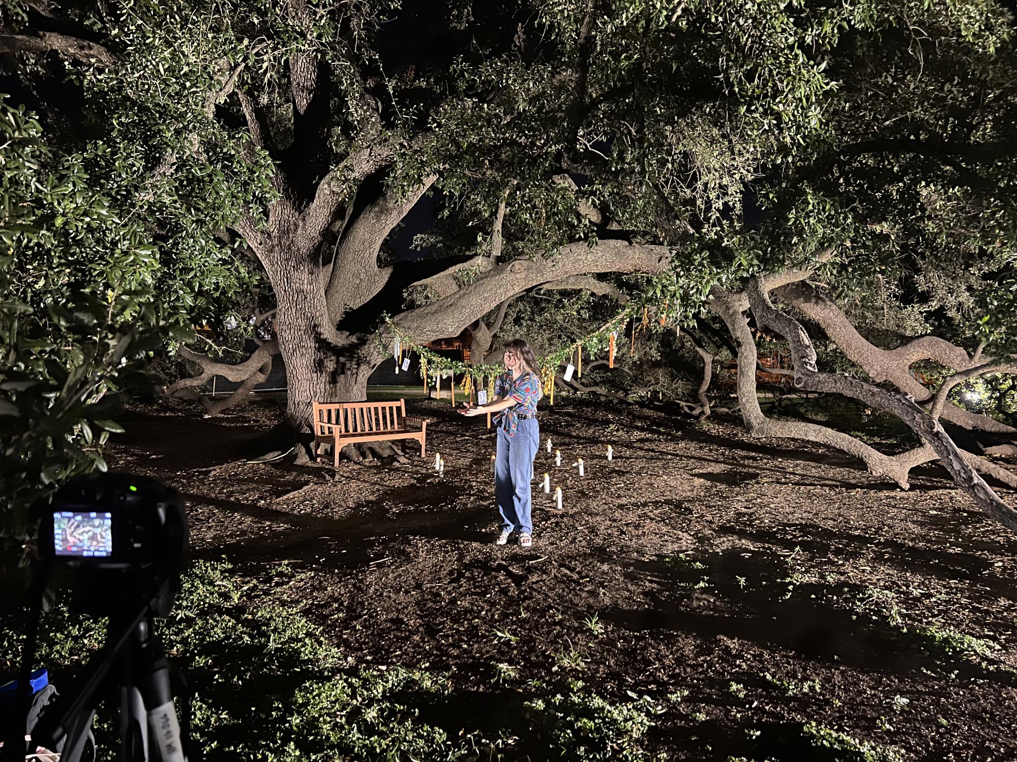 ensemble member reaches their hand out, standing in front of trees and candles