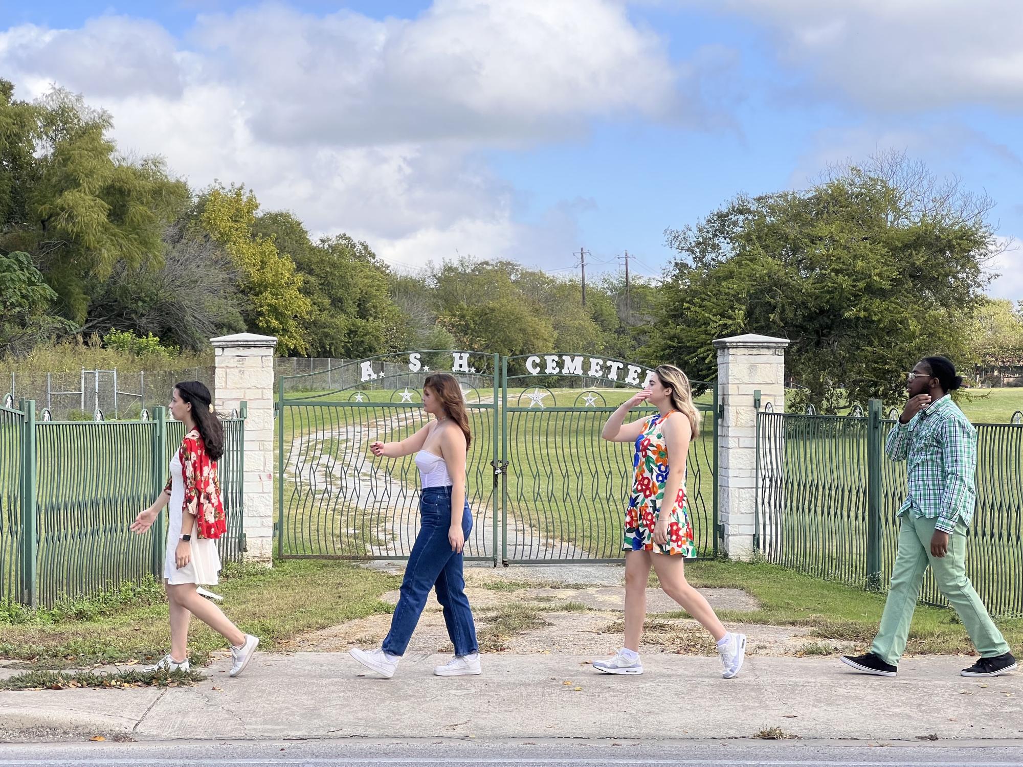 four ensemble members walk in a line in front of the gates for the A.S.H. Cemetery