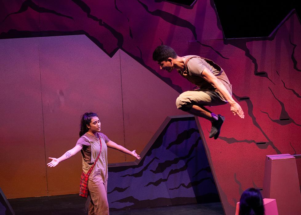 an actor jumps in the air while an actress stands below with her arms outstretched