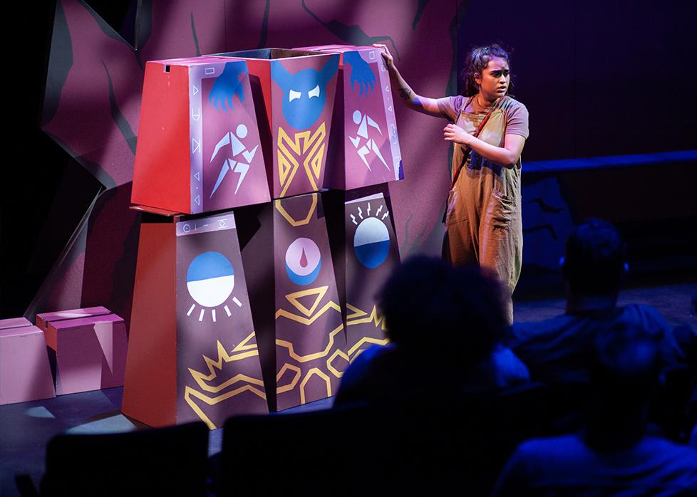 an actress puts her hand on blocks with drawings as she looks out to the audience
