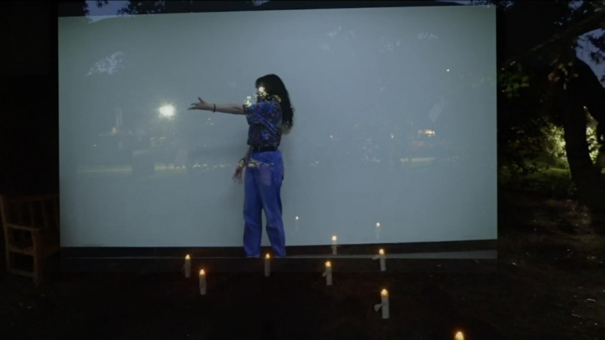 ensemble member reaches their hand out, standing in front of a white screen with an image of trees and candles layered over