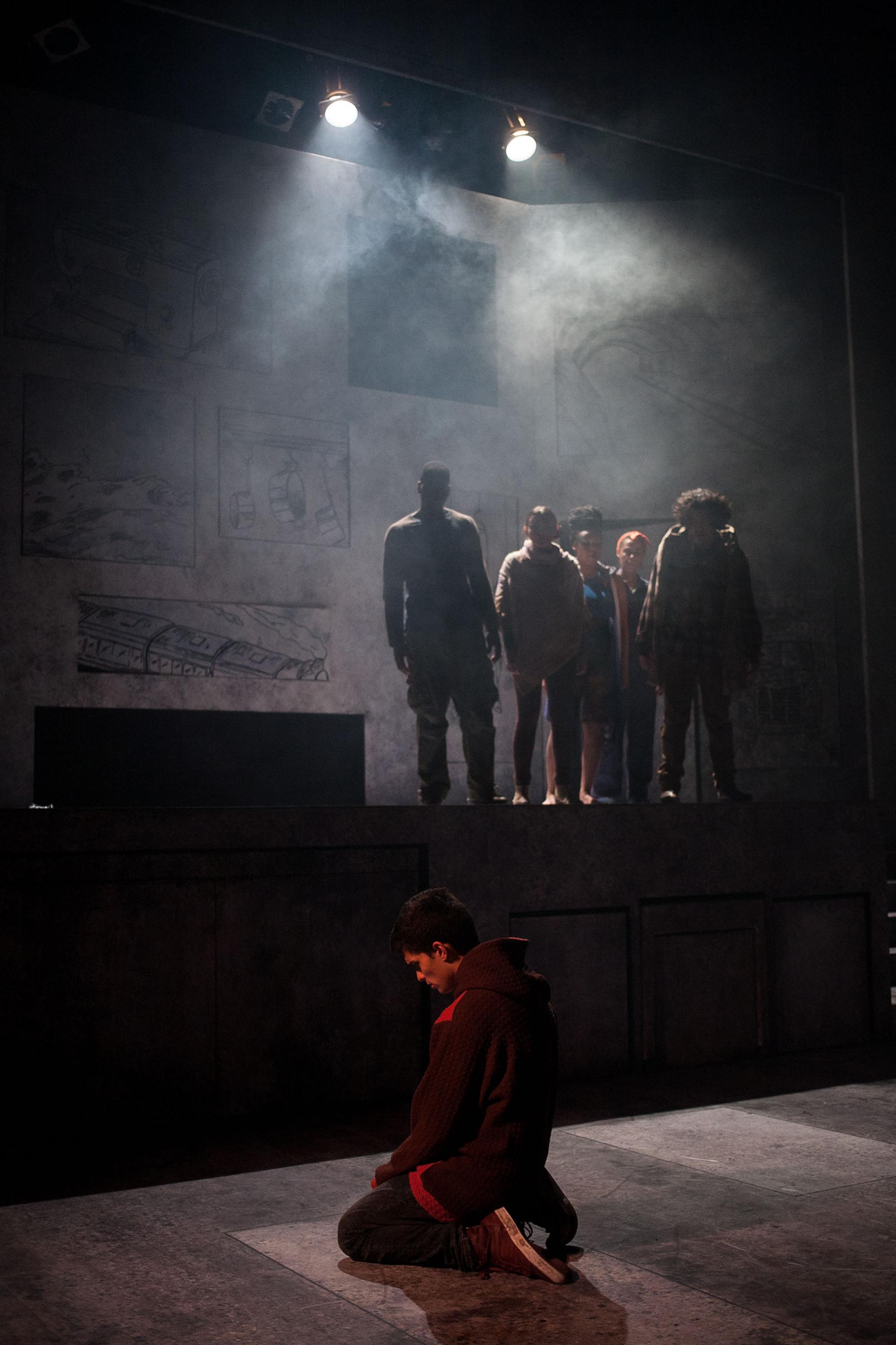 Anonymous production of actor on his knees with actors in background surrounded by haze