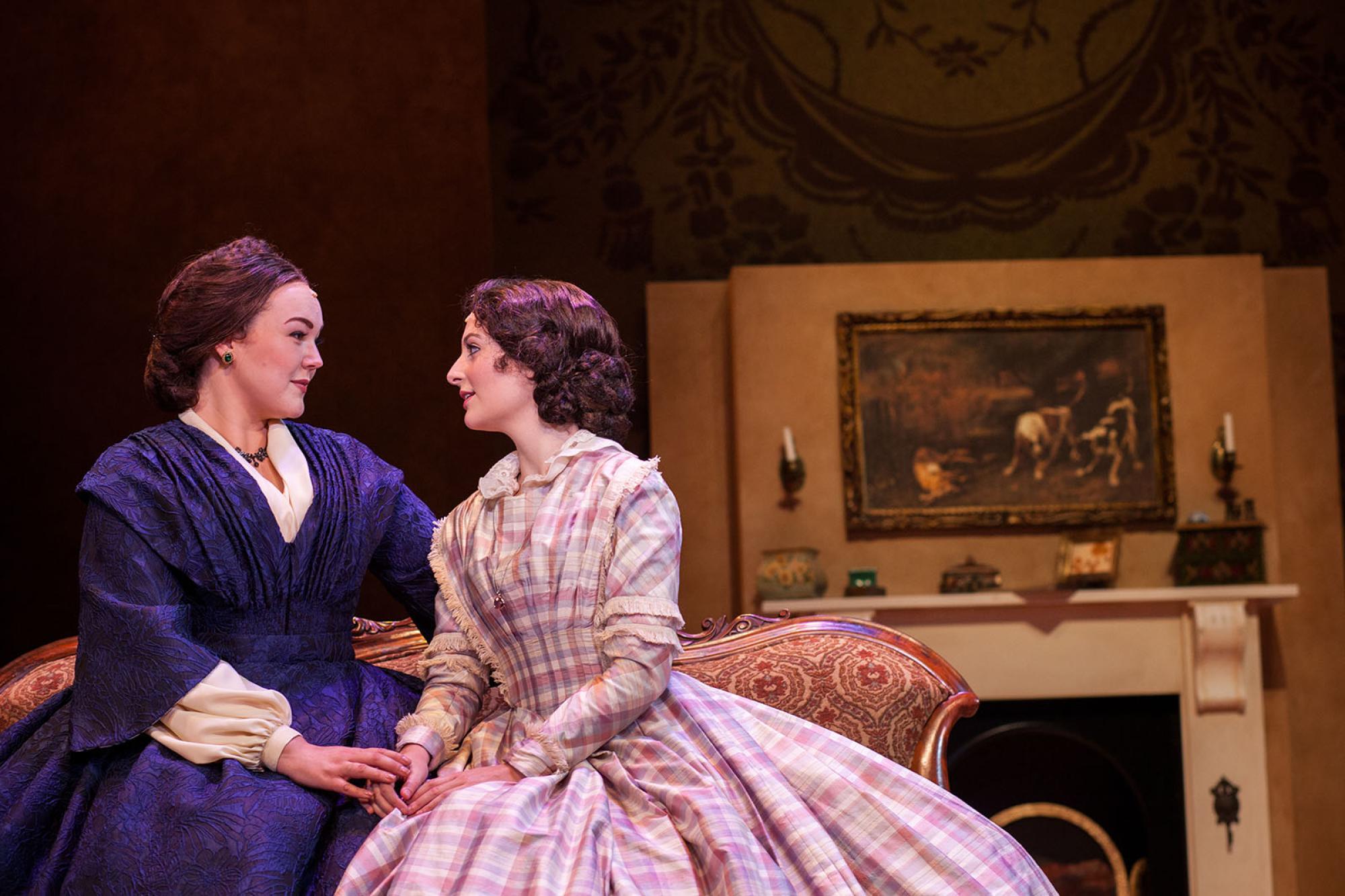 Little Women production of two women sitting on a couch in front of a great mantel