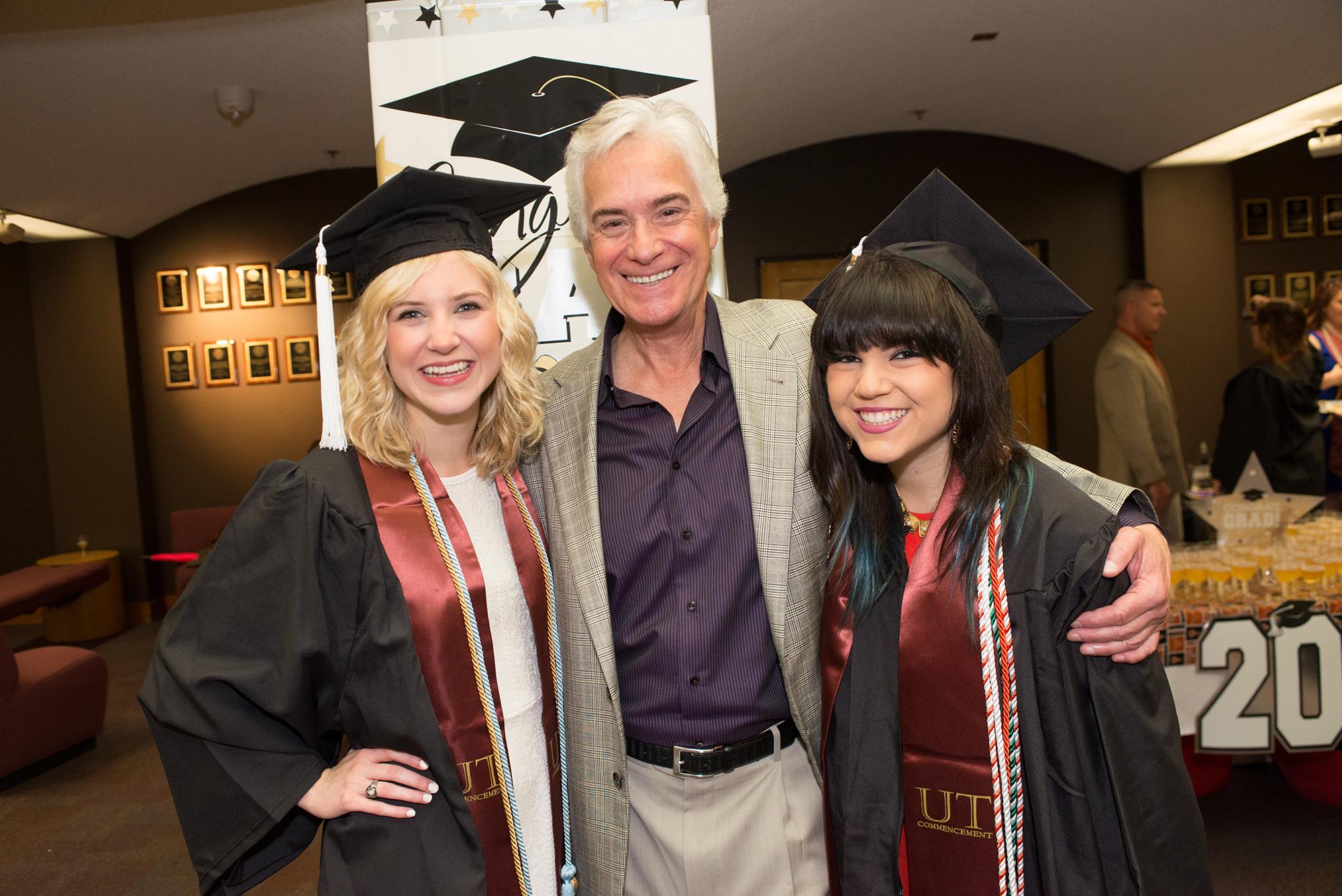 Two graduates smiling next to a man in a suit