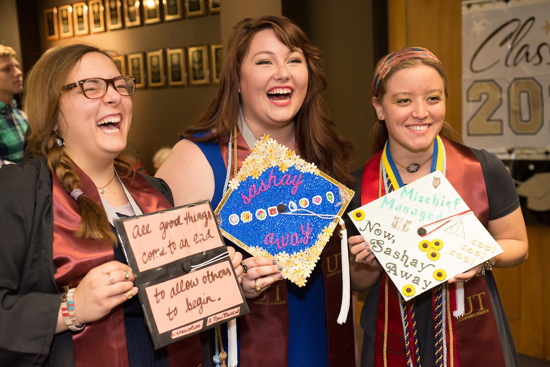 three graduates laughing and posing with their decorated caps