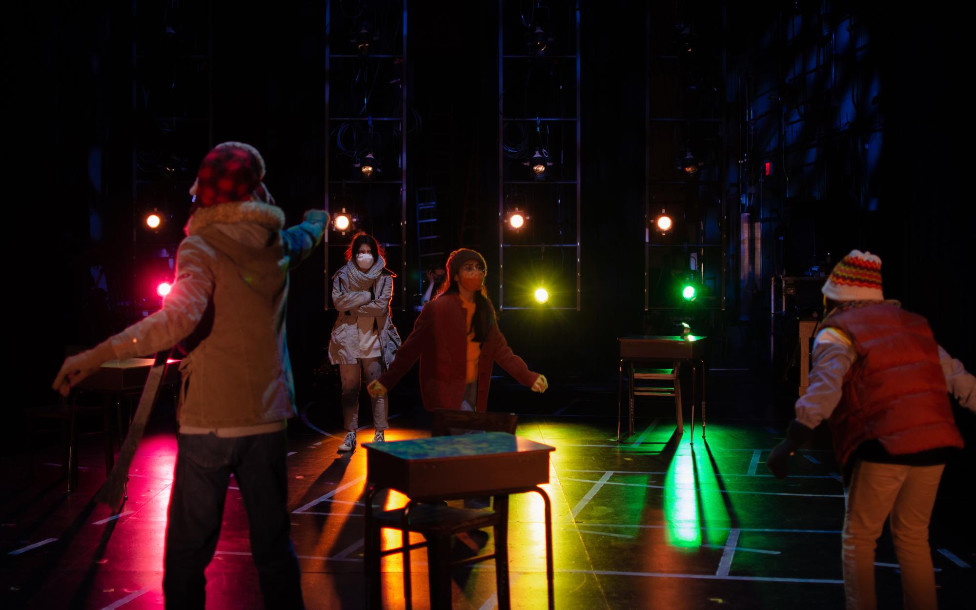 four actors portraying children playing in the winter, on a colorfully lit stage