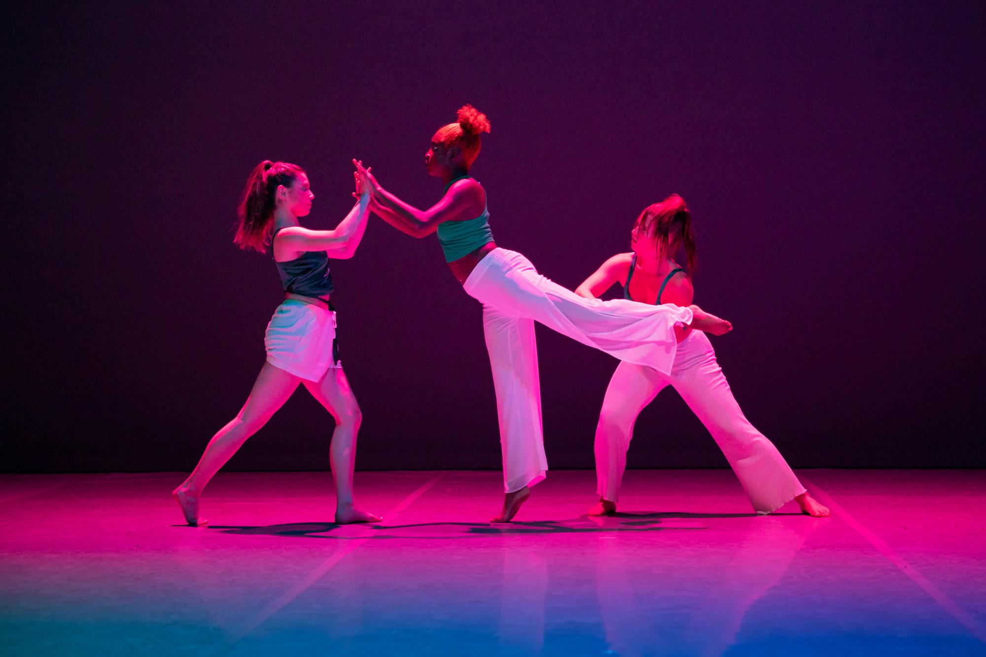 Dancers pose against each other beneath purple lighting
