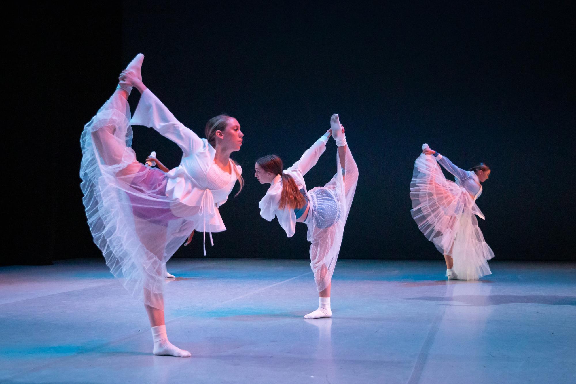 Dancers with white dresses pose with their back leg up, holding this with one hand