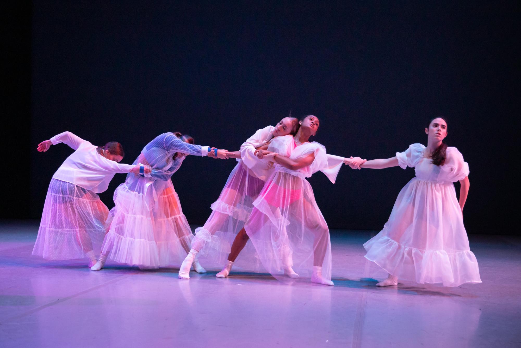Dancers in white dresses hold hands together