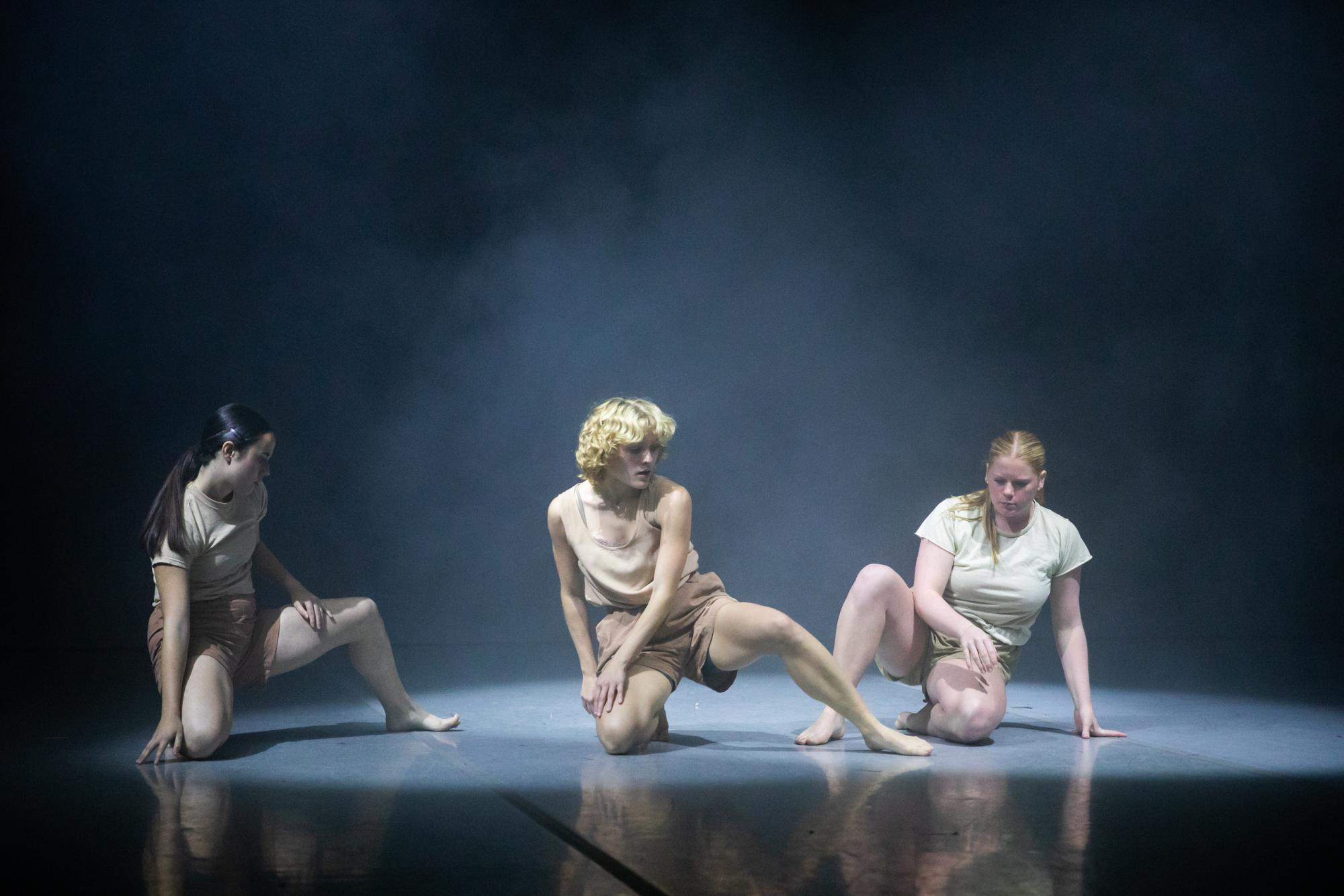 Dancers sit on stage as smoke billows around them