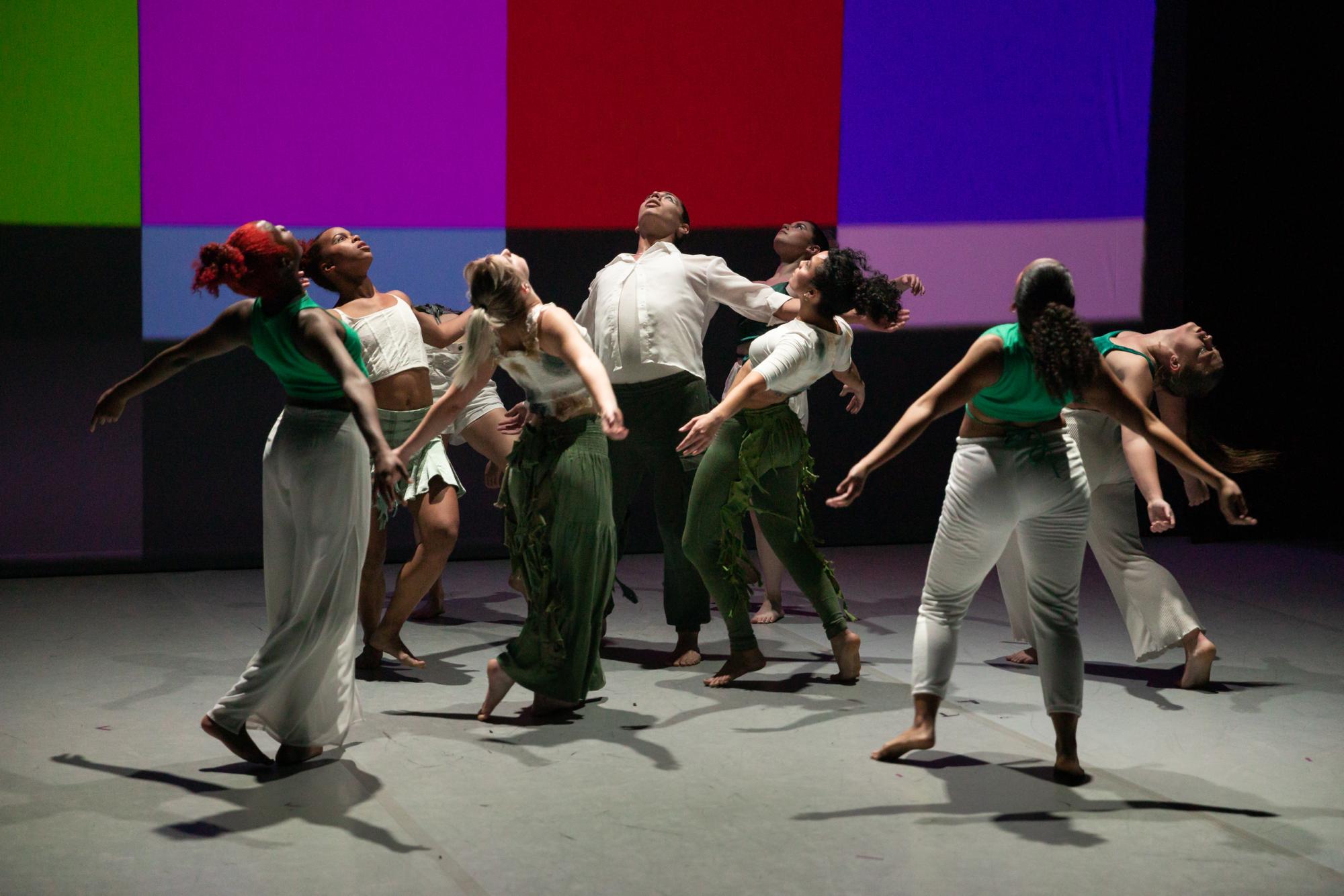 Dancers look up, leaning back with their arm outstretched against a technicolor backdrop