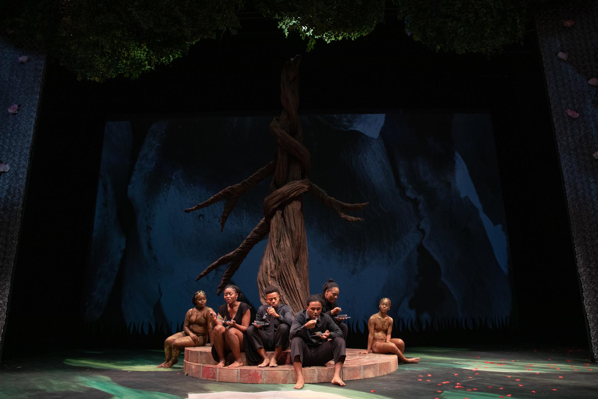 People wearing gold and black lounge under a giant tree