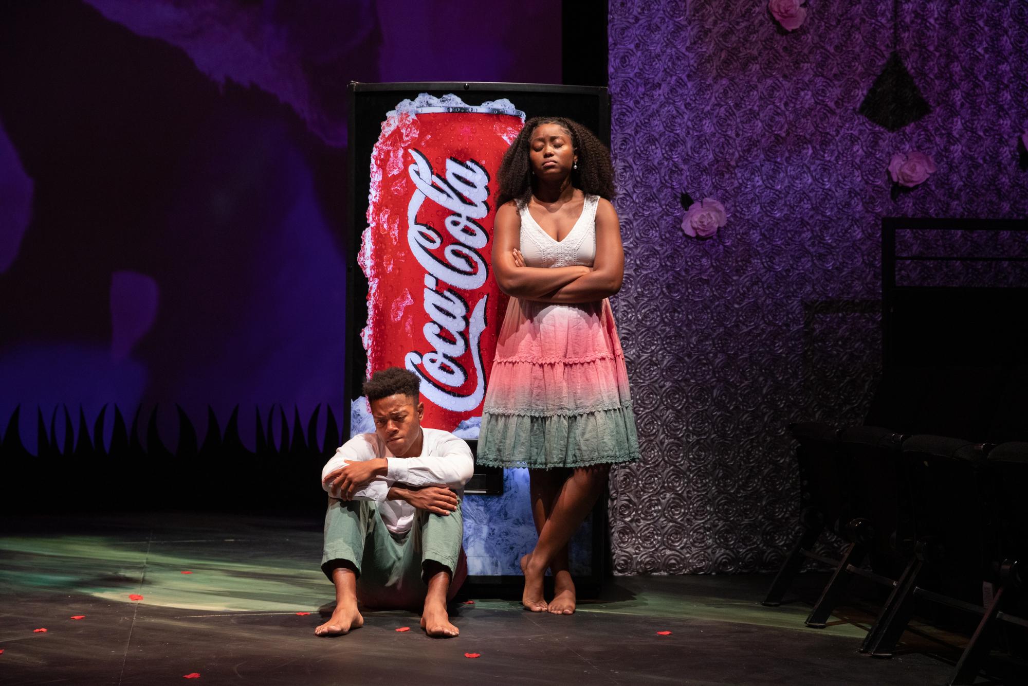 A seated boy and a standing girl lean on a vending machine