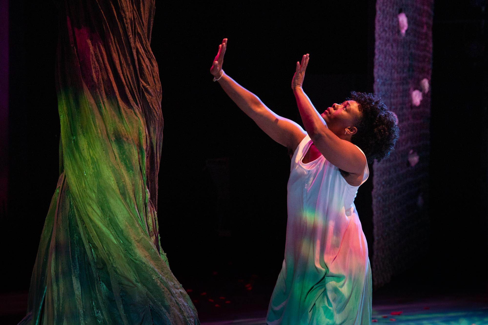 A woman hold her hands up to a glowing tree