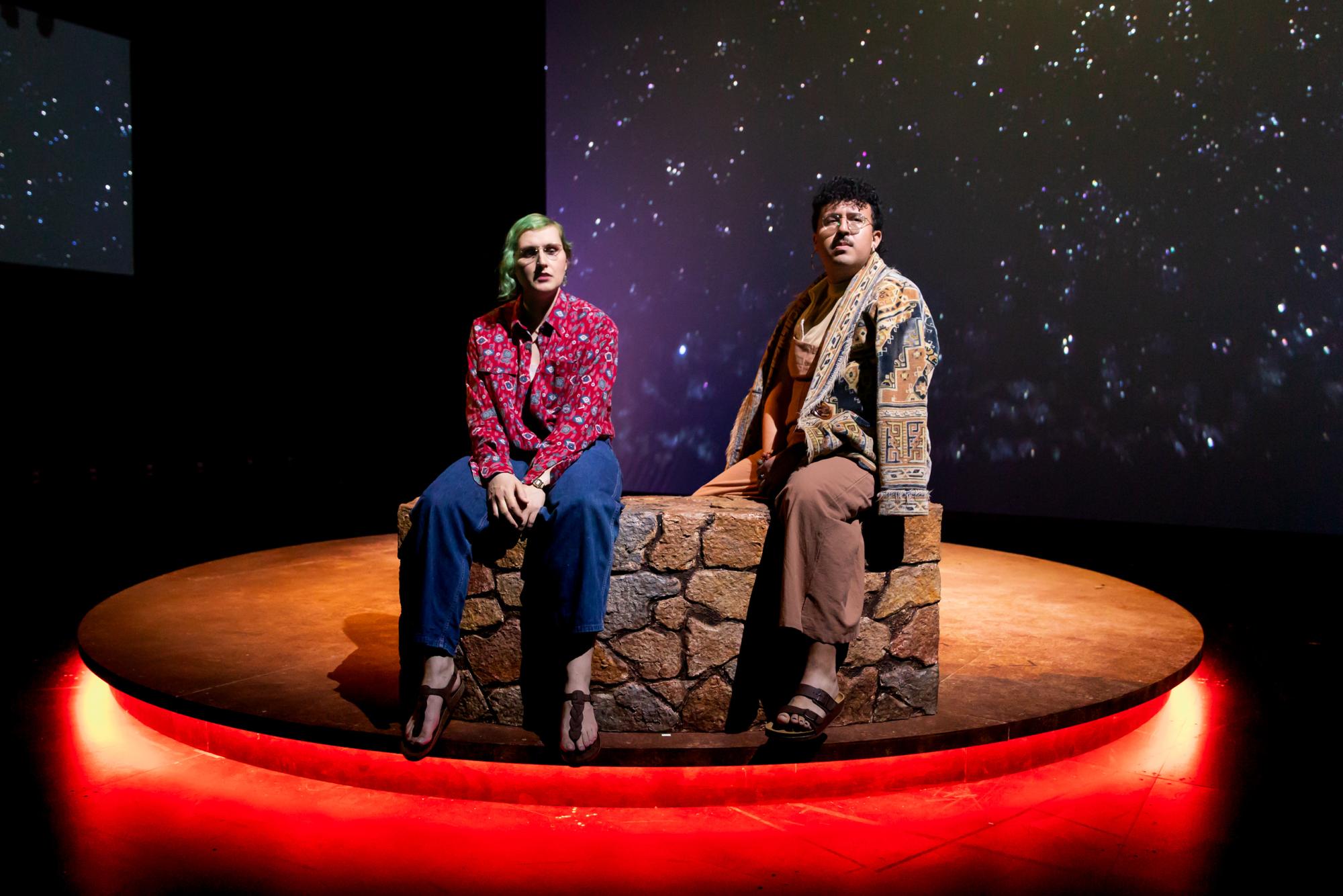 Two people sit on a desert wall gazing at the stars