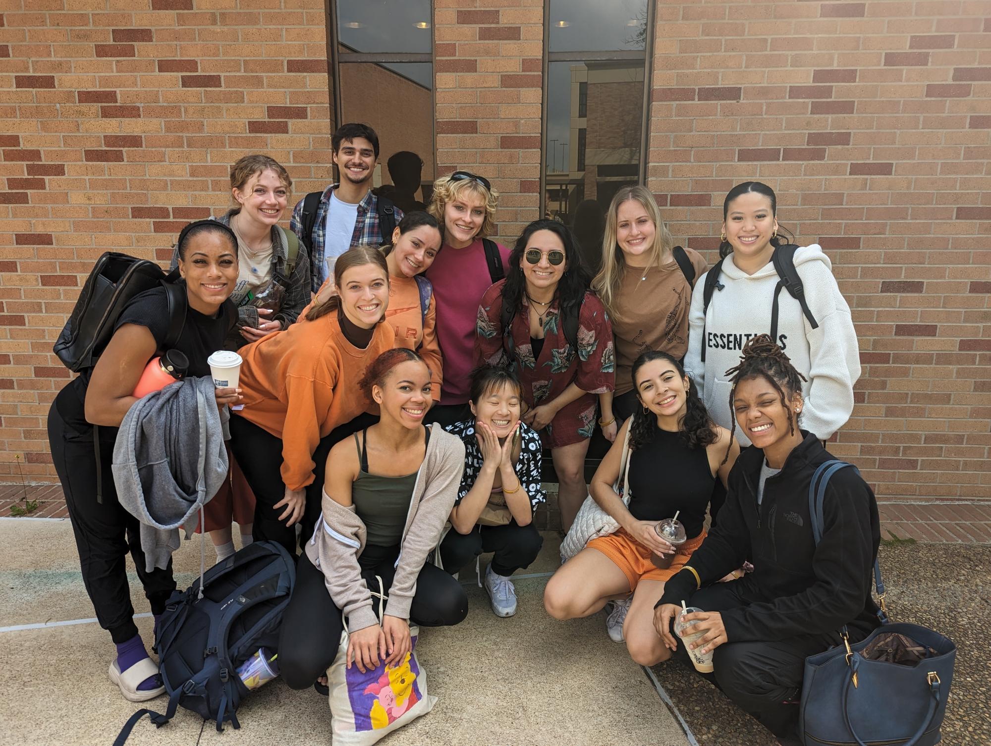 13 UT dance students smile together in front of a brick wall at the ACDA regional conference