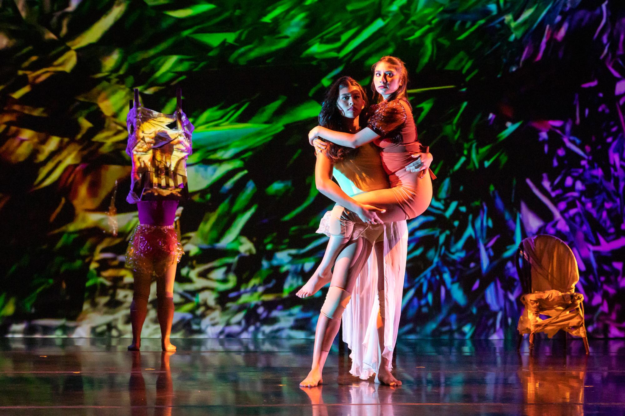 A dancers holds another against a multicoloured background