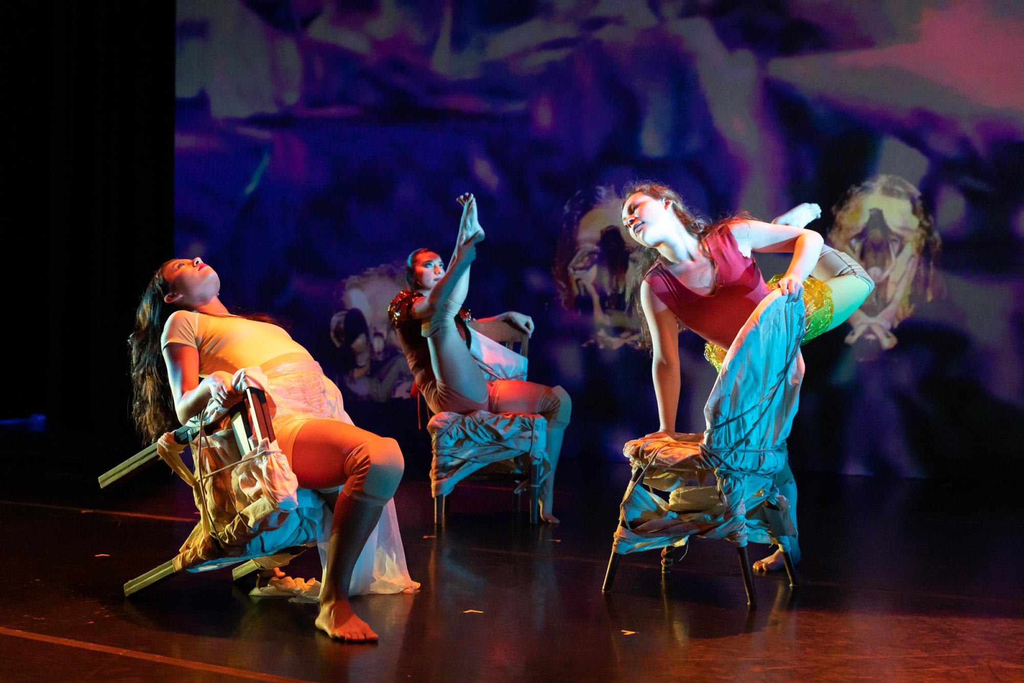 Three dancers pose on colourful chairs