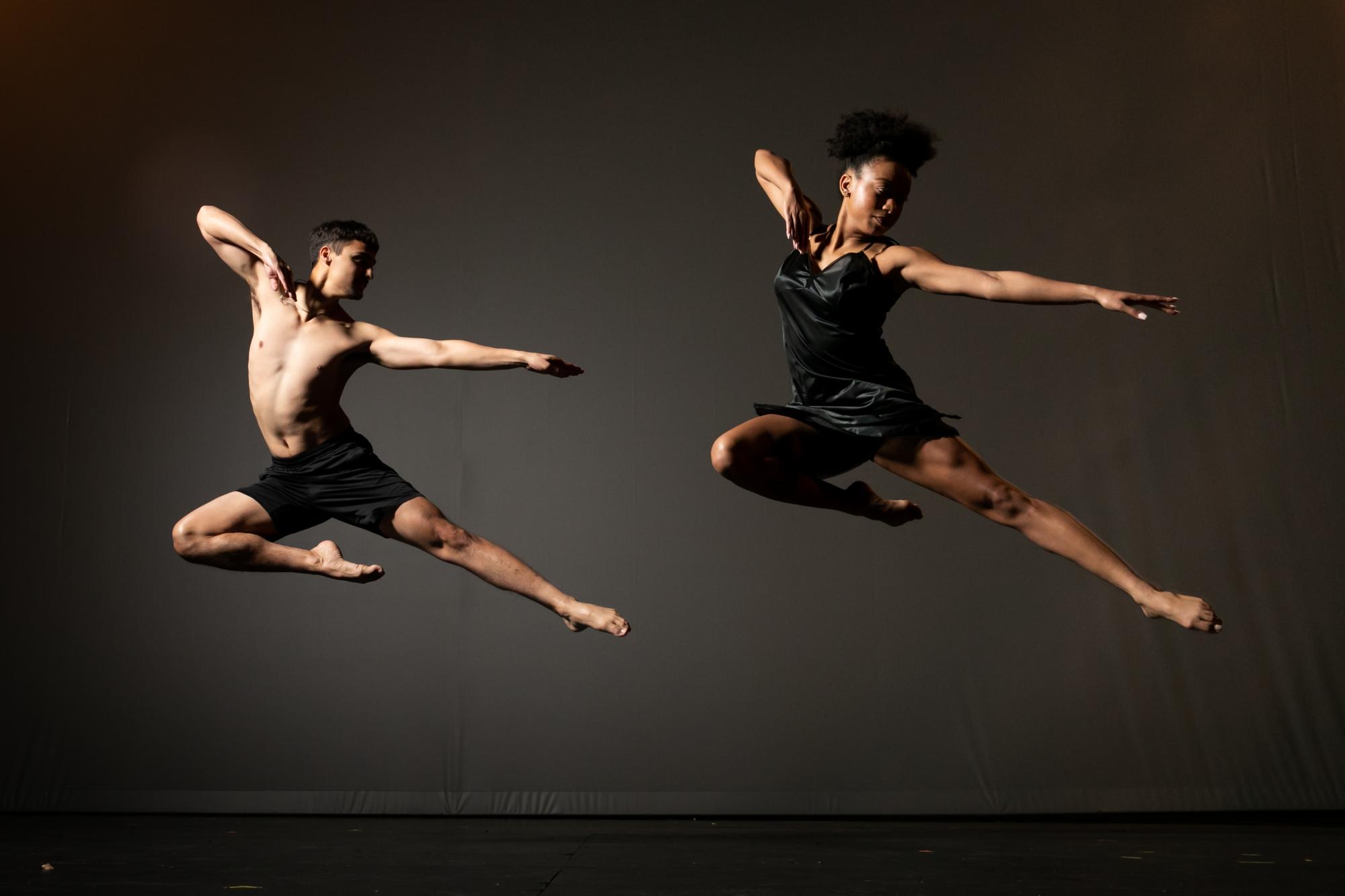 Two dancers caught mid-jump with their left legs and arms extended and their right arms and legs bent