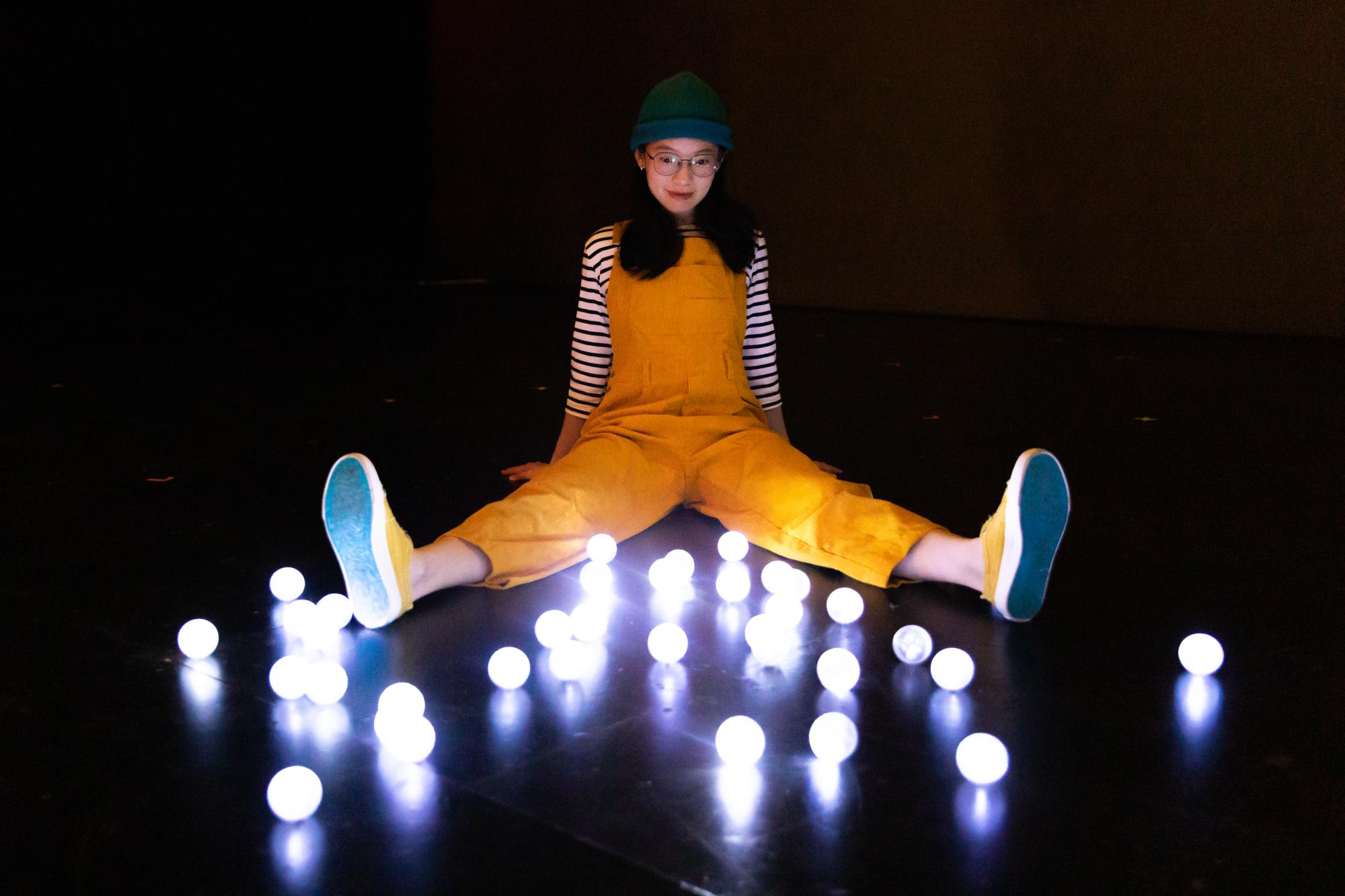 An actor in yellow overalls sits in front of glowing white spheres