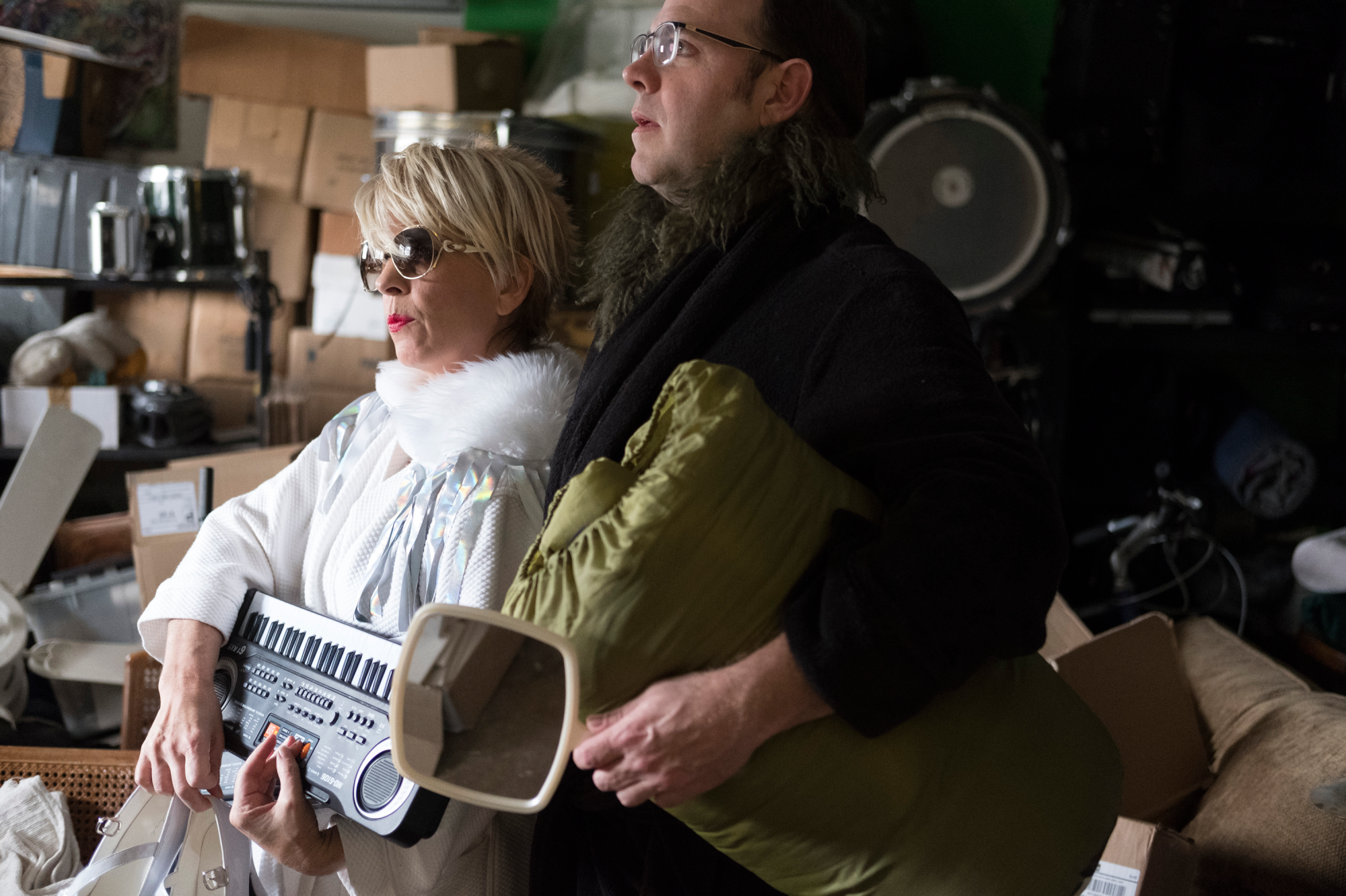 Actor Lana Lesley wearing a blonde wig and holding a small keyboard, standing with a fellow performer during a production with the Rude Mechs