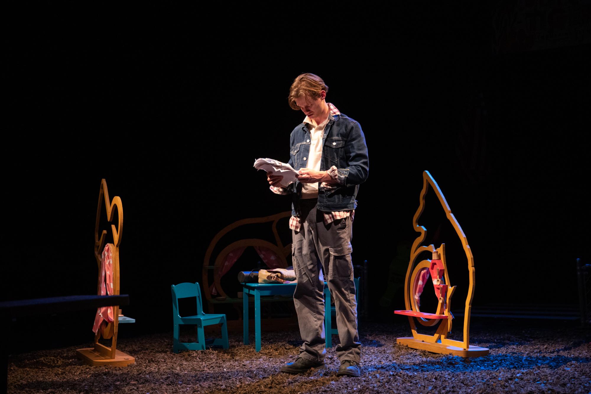 Actor Oliver Aaro as Arthur stands surrounded by the magical playground equipment he built looking at a flyer for armored backpacks.