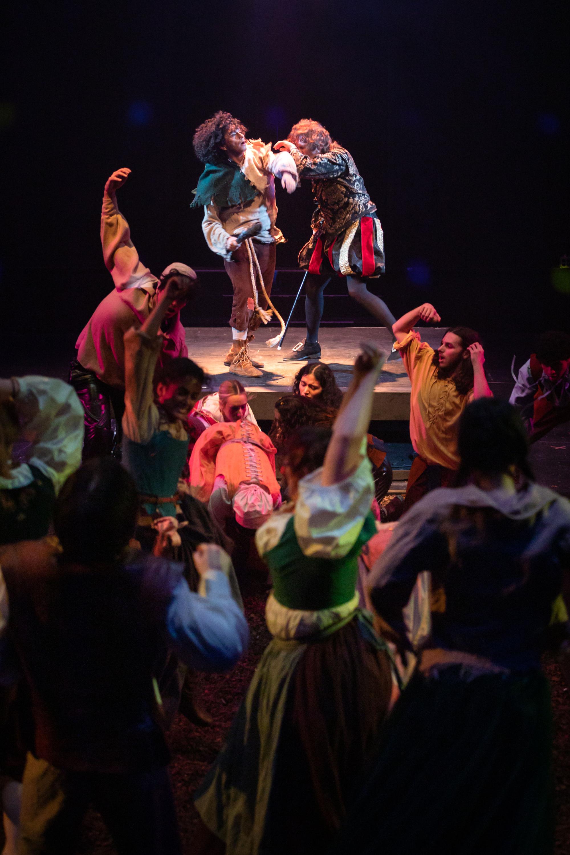 Adam Flores Jr. as Marcus tussles with Joe Adkins as Feudal Lord on a platform looking over a crowd of afflicted choreomaniacs.