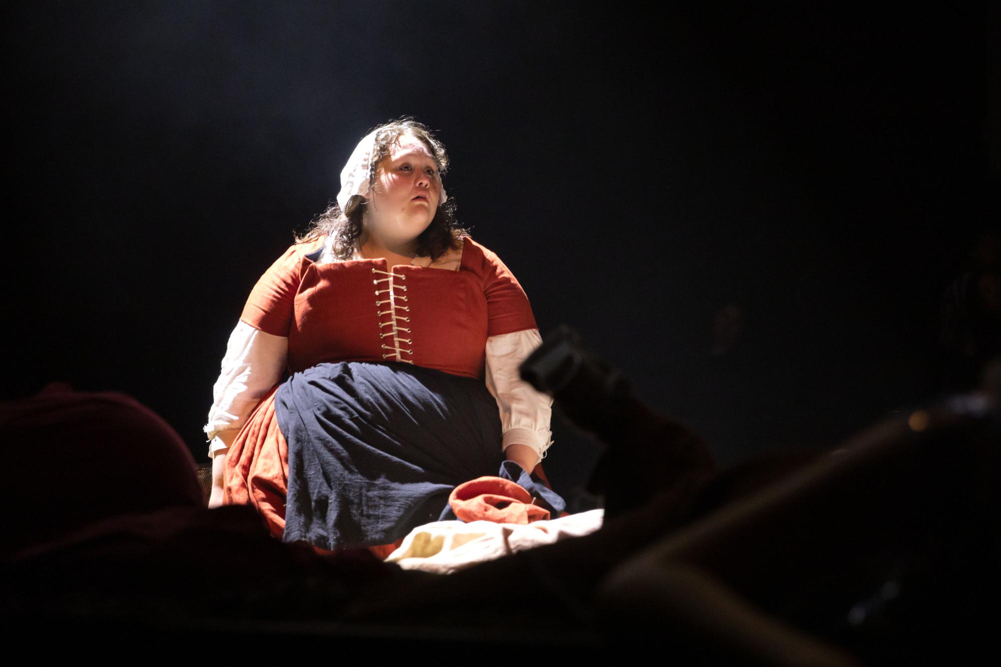 Angela Mata as Frau Betty sits basked in a white light, looking out over a sea of dead choreomaniacs and potatoes... lots of potatoes.