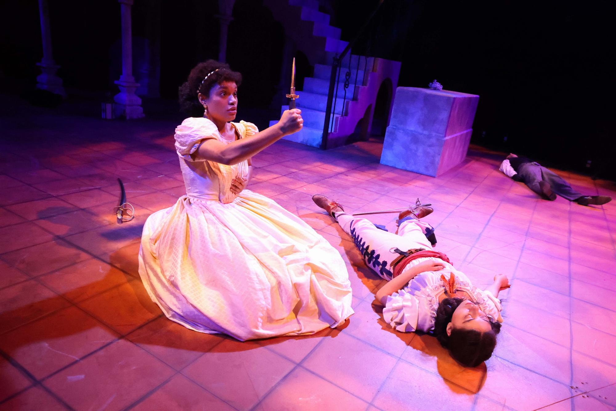 Juliet holds the dagger up to her chest as her Romeo lays on the floor next to her. Stricken by grief, the age old tale once again comes to completion as young Juliet prepares to take her life.