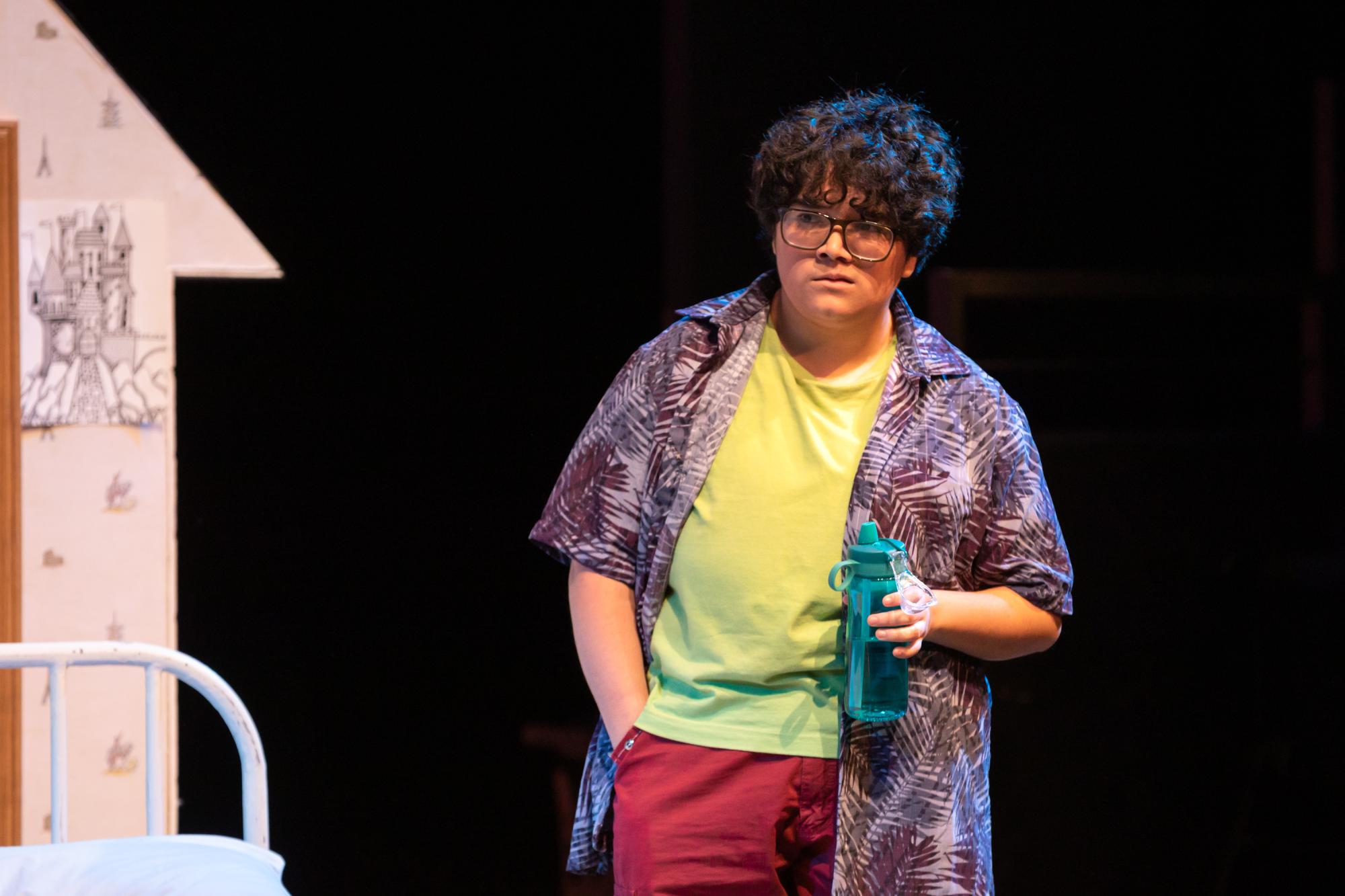 Leo Martinez played by Gibby Reyes stands, looking dejected with a water bottle in their hand. A water bottle that they are never seen without due to their chronic illness. One that debilitates them from participating in the school election, and... the quiz show.