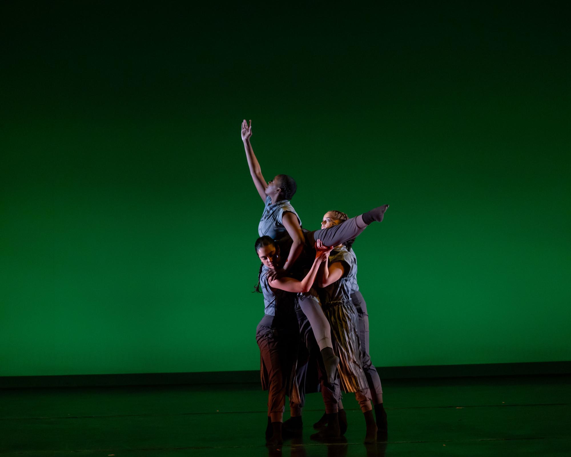 3 dancers of Points of Intersection hold a forth dancer in a lift, where the lifted dancer reaches toward the sky with a leg and foot extended to the side. 