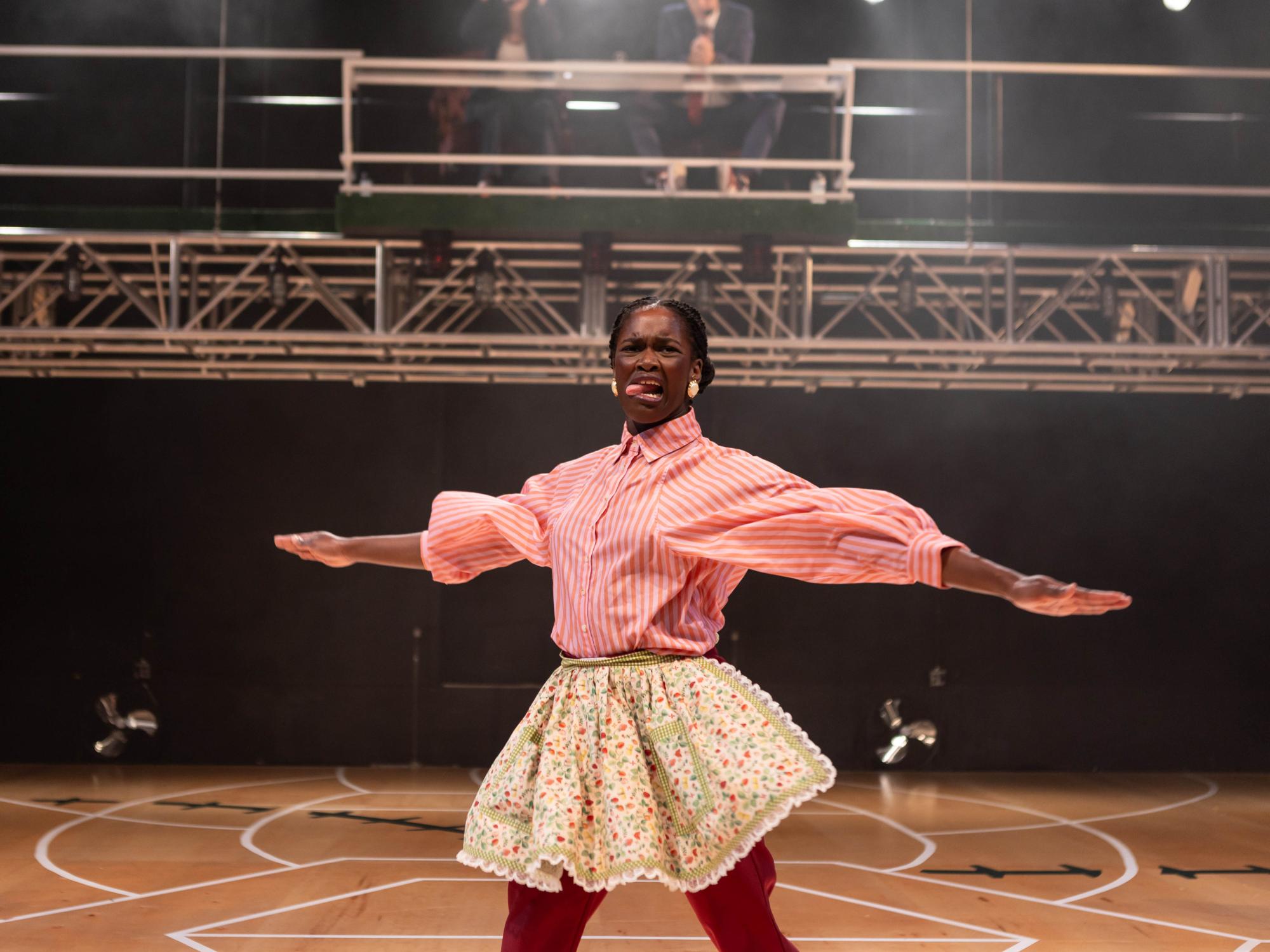 The oldest sister, Trifle, played by Oyin Ojomo swings her arms from side to side, sticking her tongue out. She is depicting the sport of cleaning up dishes.