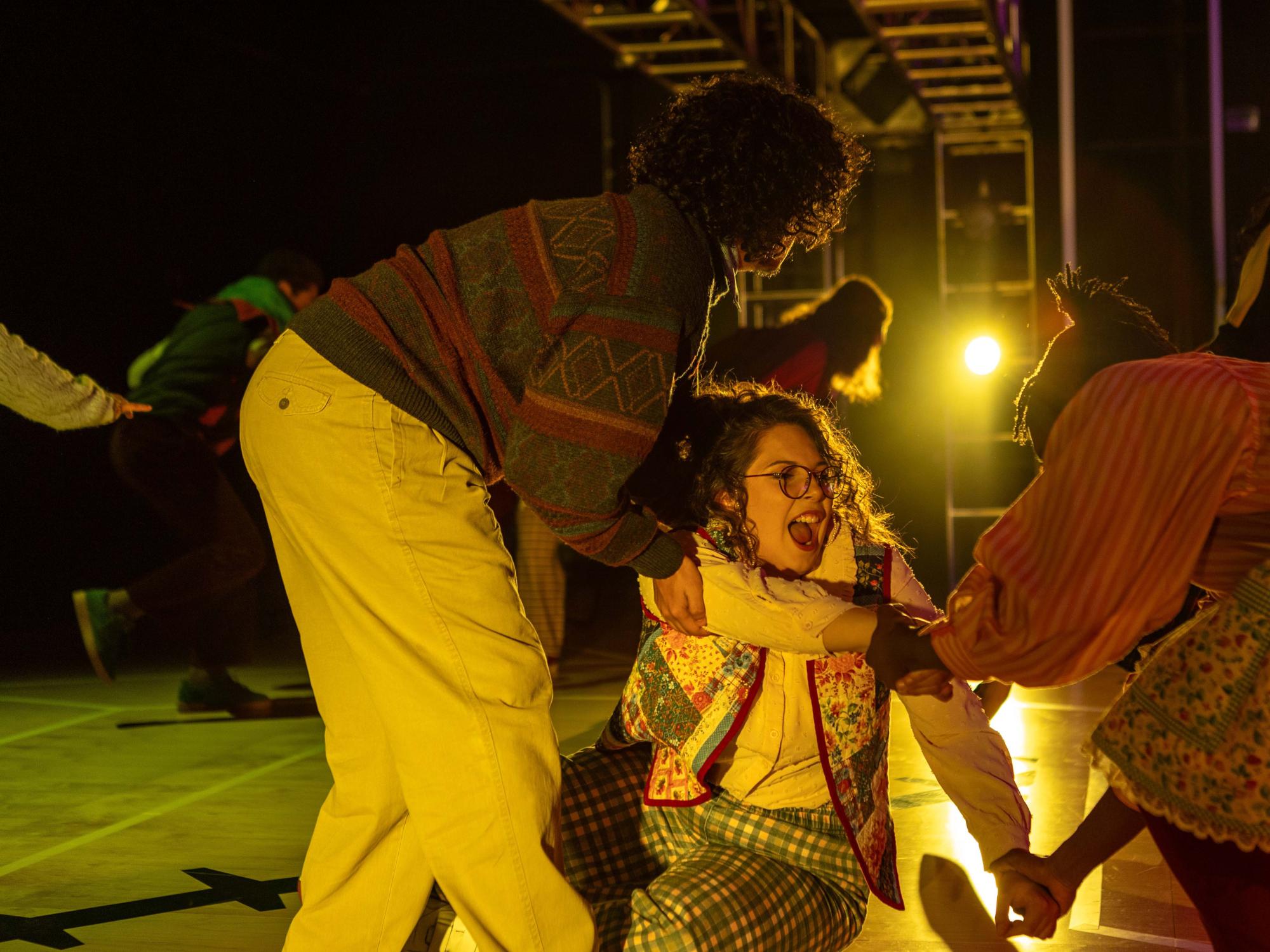 Cheesecake, Emerson Hartman, is on the ground after running for her life from the herd of uncountable great-grandbabies. Her husband, Ned, Adam Flores Jr., and her sister Trifle, Oyin Ojomo, bend down to help her up.