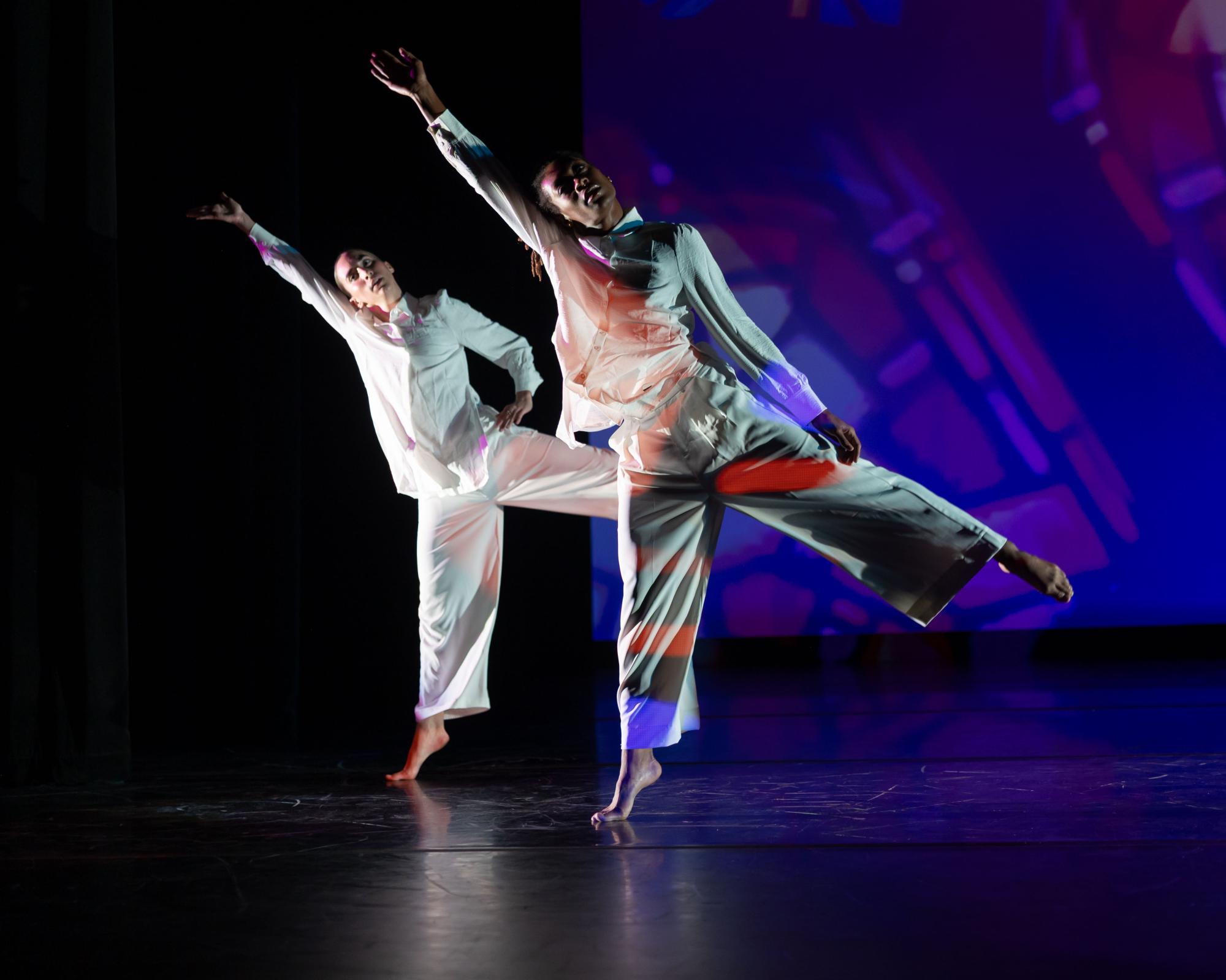 Agape Love takes the stage, with two dancers cloaked in white with rainbow projections on them. Their legs and arms are in a diagonal.