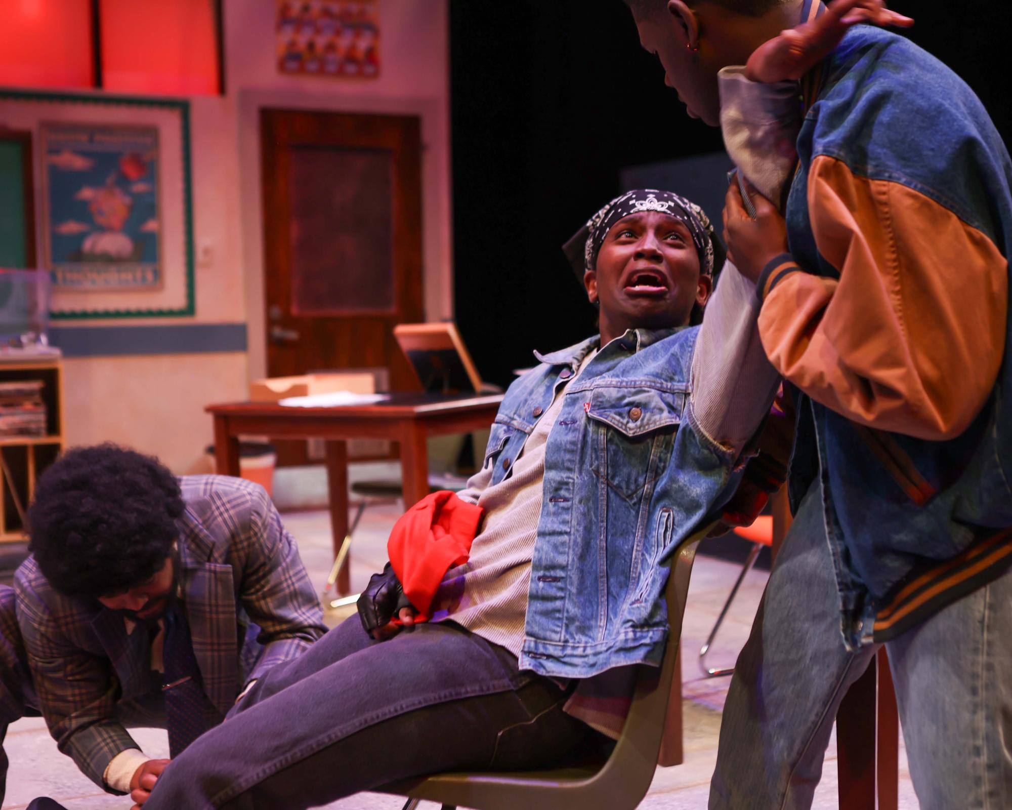 Finding refuge in Touchless's classroom, Isaiah, played by Trevor Gatabaki, and Reggie, played by Khalia Sacko, run from their gang activities. There is glass thought to be a bullet in Isaiah's leg.