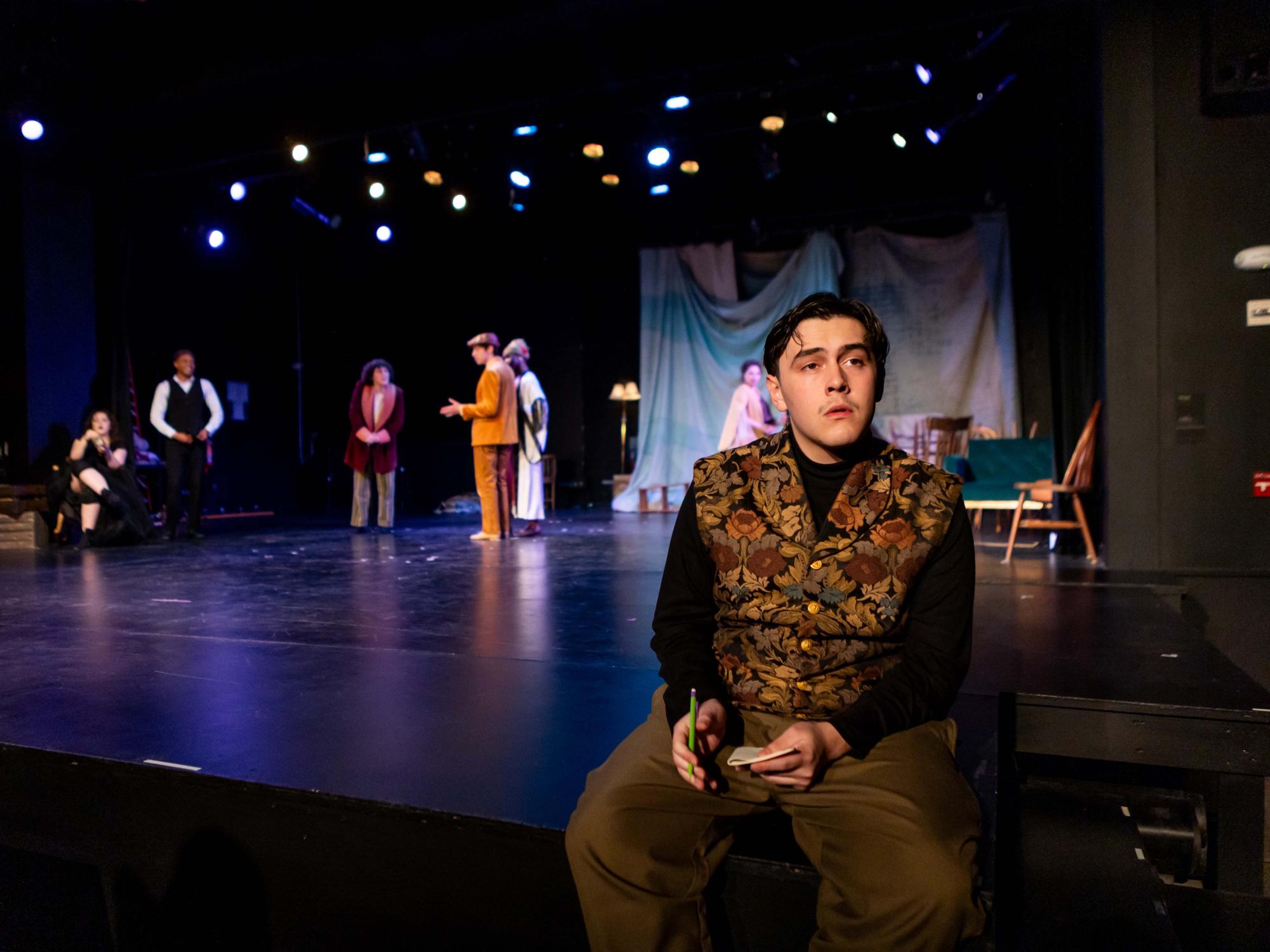 Diego Rodriguez as Trigorin sits on the edge of the stage staring off into an imaginary pond/lake. Majority of the cast stands behind him having a chat.