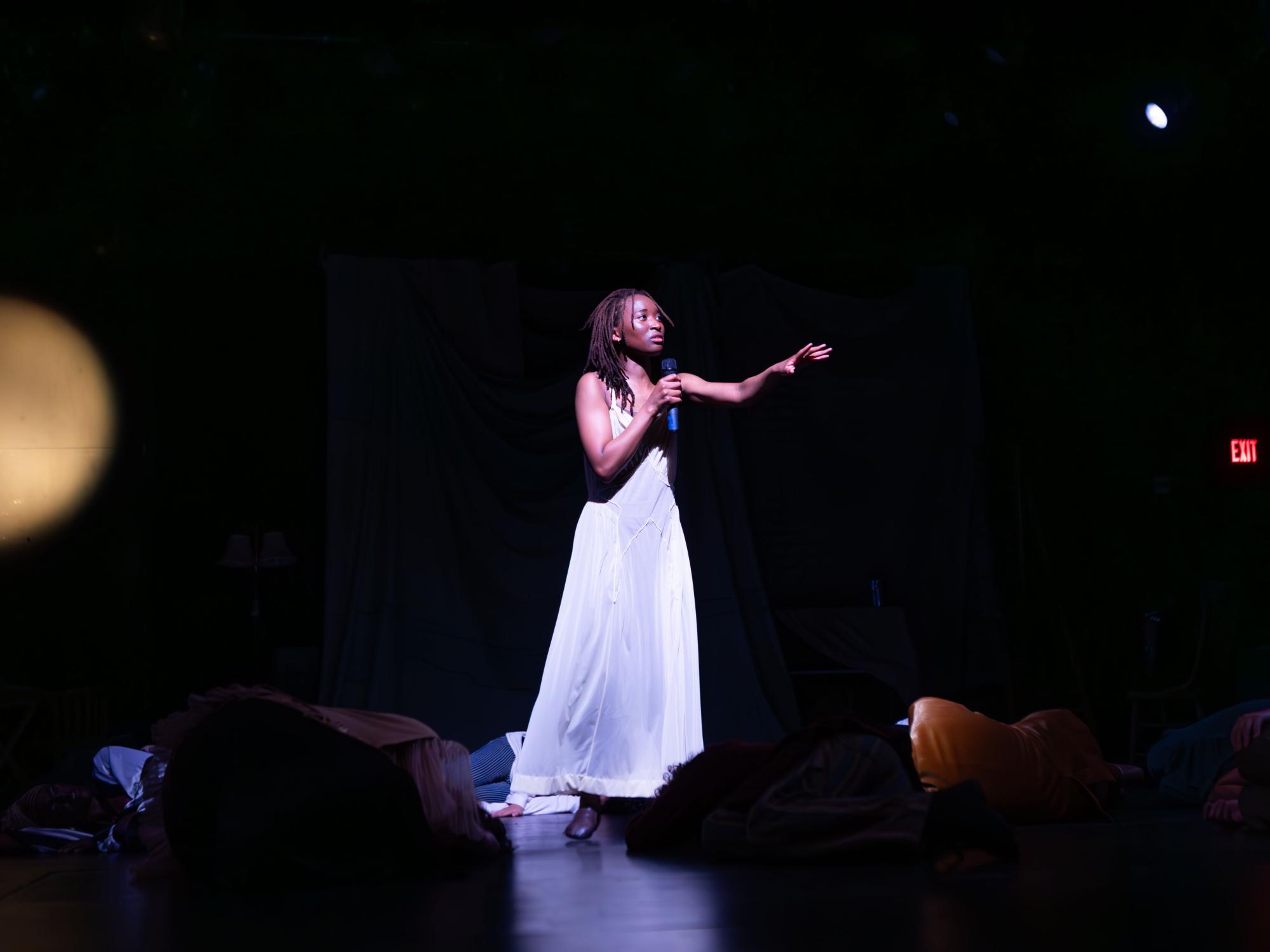 In one of the new theatrical forms explored, Eian Johnson as Nina stands center stage listing animals in a spotlight. The rest of the cast has decayed to dust on the floor.
