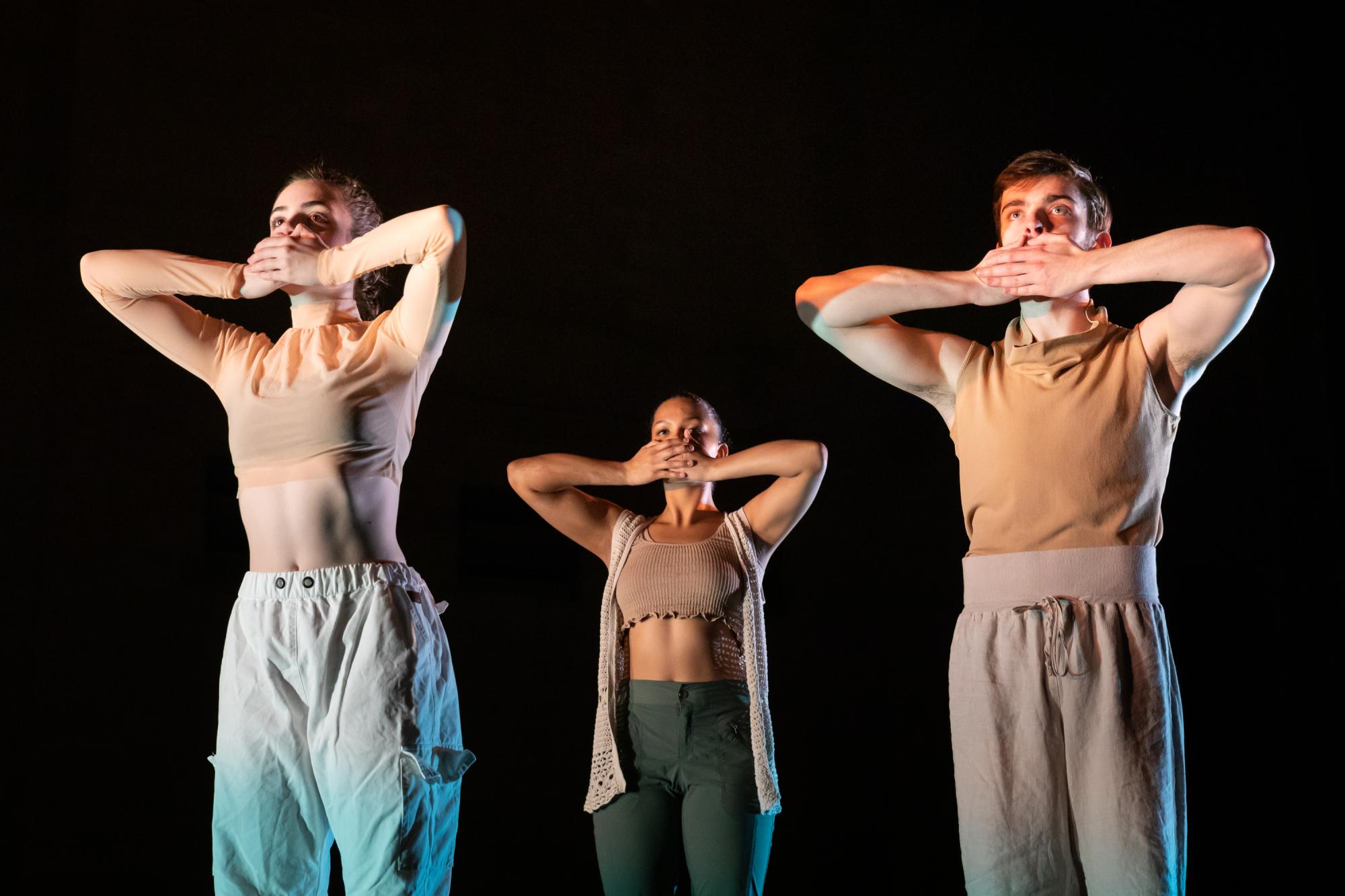 Covering their mouths with their hands, the dancers stand still in silence