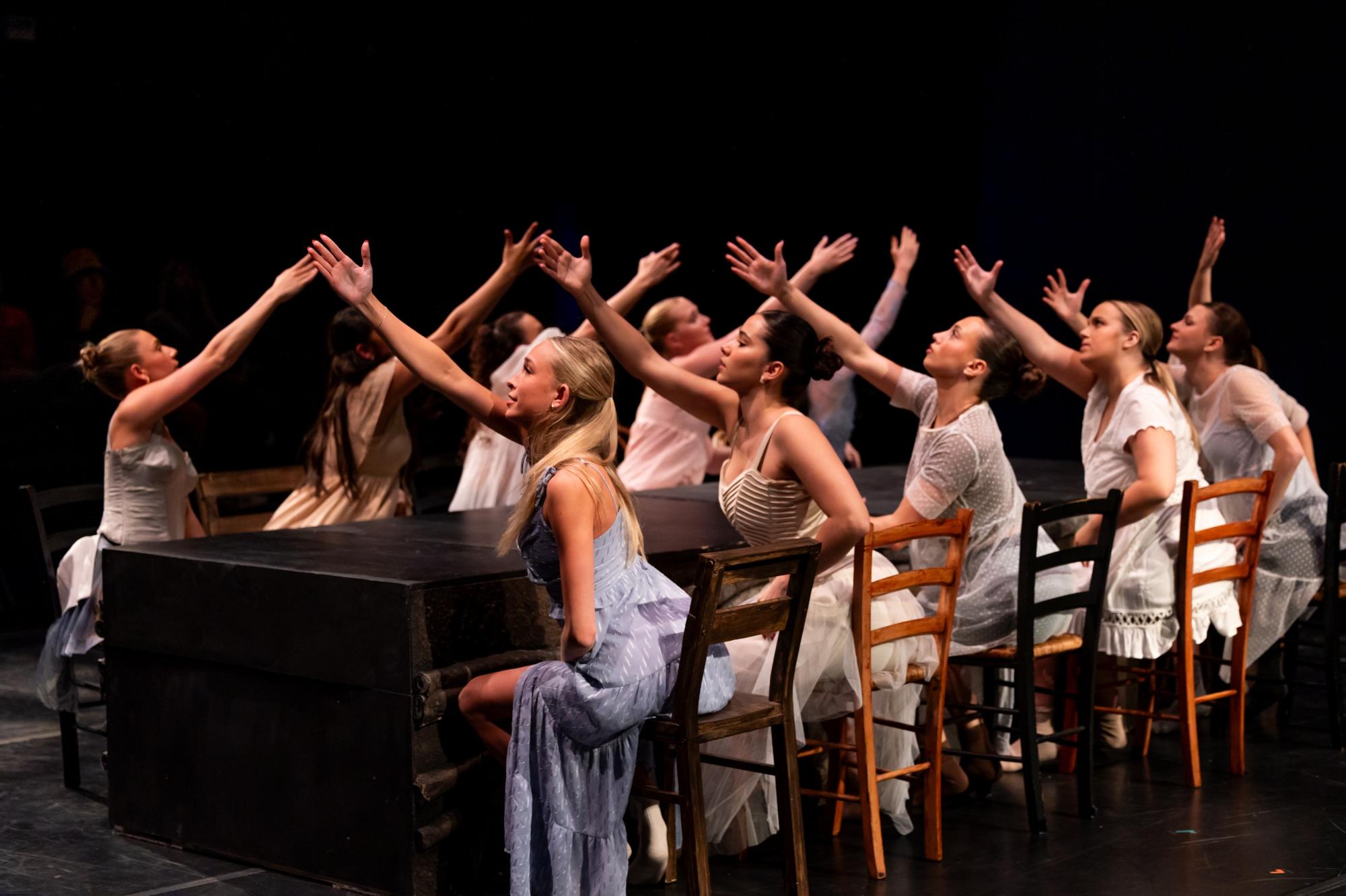 Photo of dancers sitting opposite each other on a table with raised hands