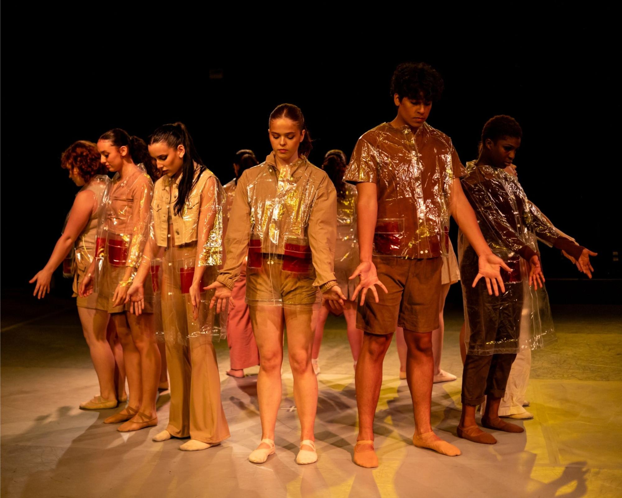Photo of group of dancers facing outward in a circle with their palms out in orange light