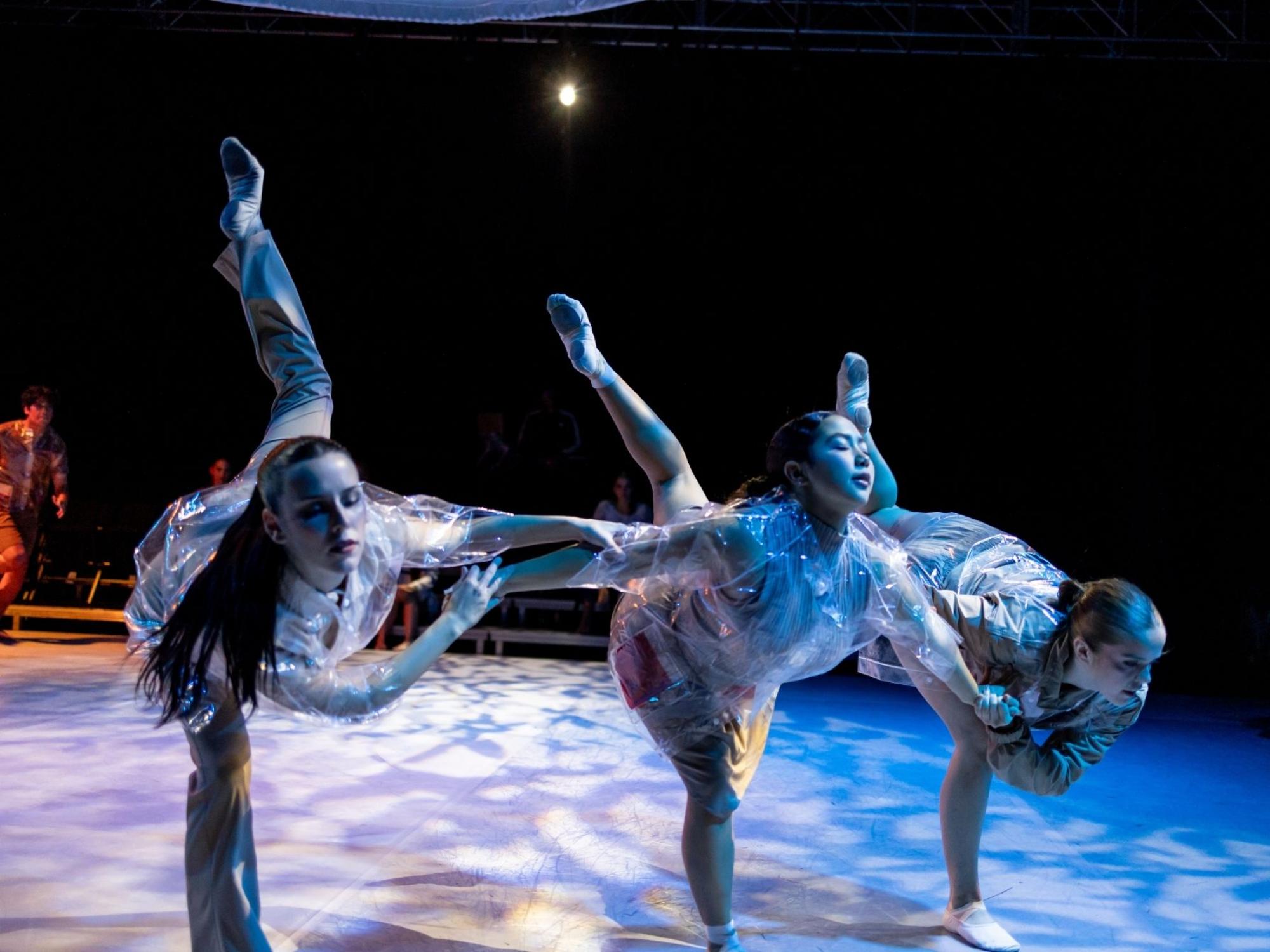 Photo of three dancers bent forward with legs extended behind them