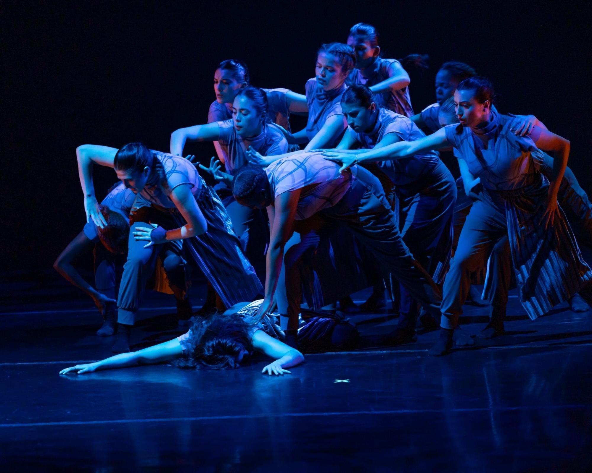 Photo of group of dancers lit in blue reaching towards eachother