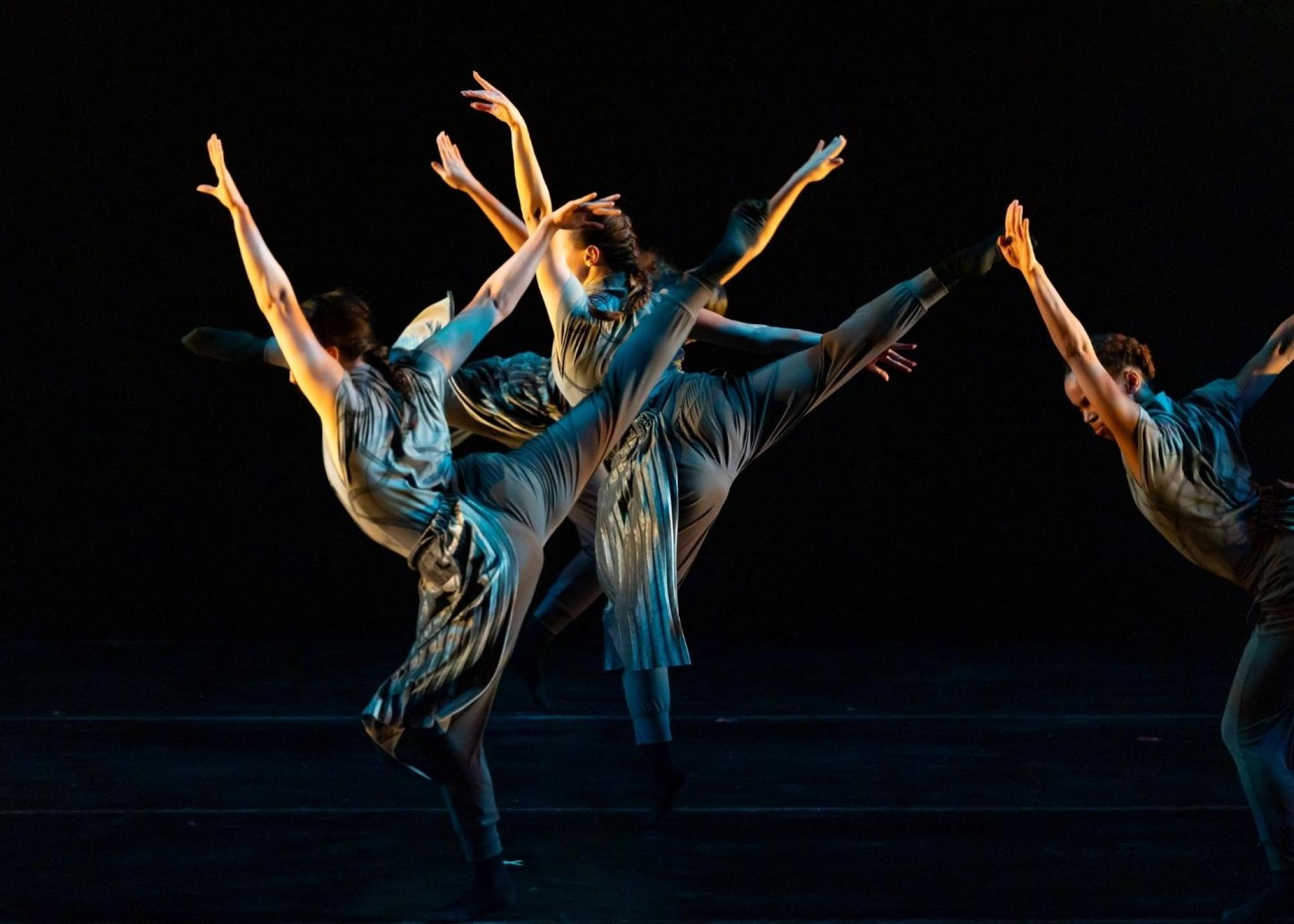 Photo of dancers on one leg with their arms and free leg up in a v shape in metallic gray clothing