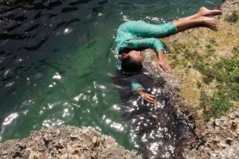 woman in a green dress holds on to a rock while partially submerged in water