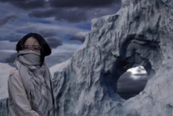 actress in all gray with her scarf over her nose and mouth looks concerned, sitting in front of an iceberg