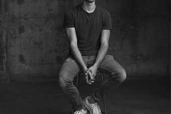 man sitting on a stool in front of cement wall 