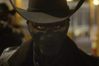 man wearing all black with a full-face mask and a cowboy hat