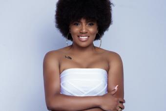 woman with black, curly hair styles in an afro wearing a white dress and large hoop earrings