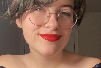 woman with short brown hair wearing round glasses and red lipstick